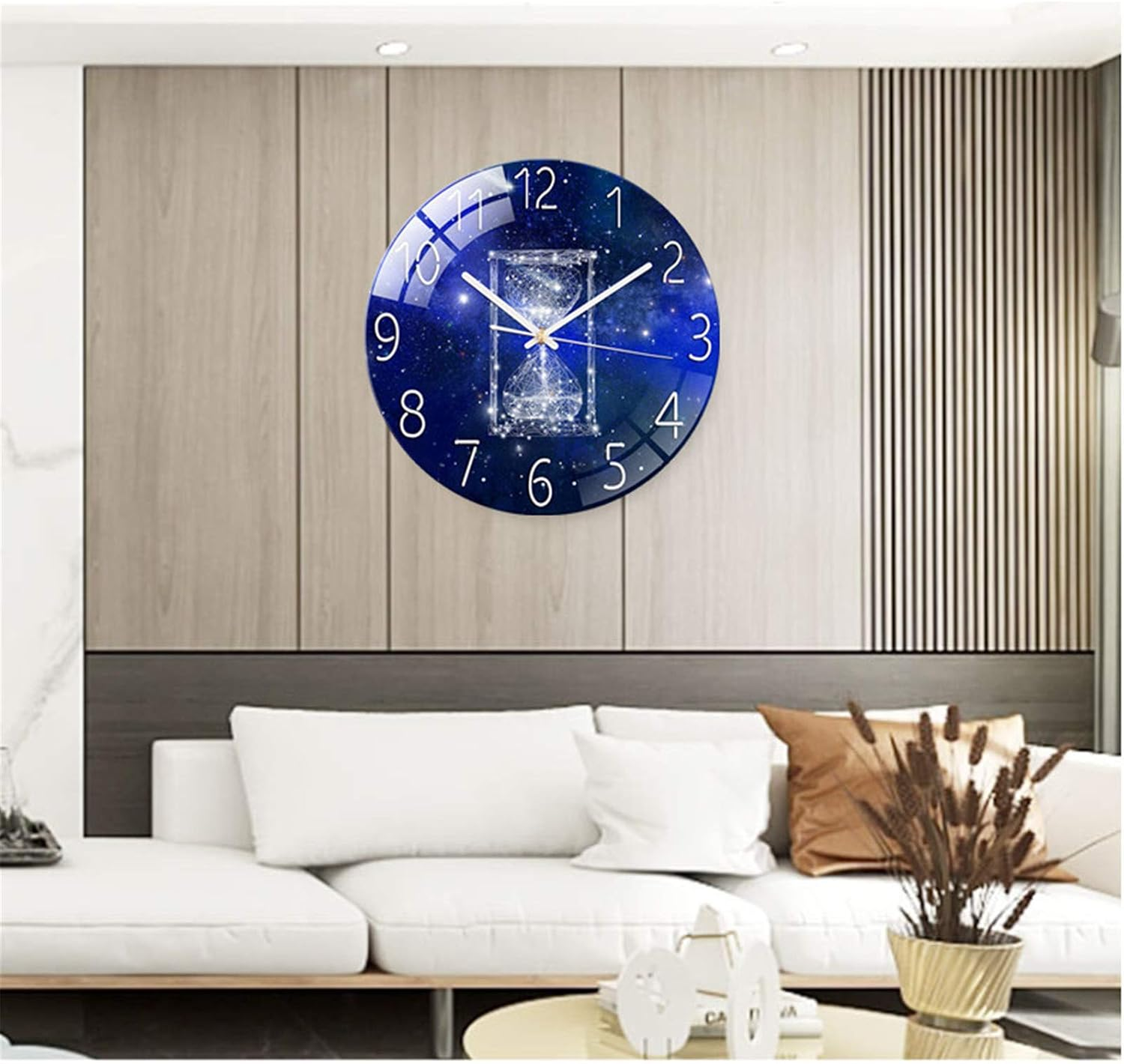 Eine blaue Wanduhr mit Weltraummotiv und Sanduhr hängt über einem weißen Sofa in einem Wohnzimmer.
