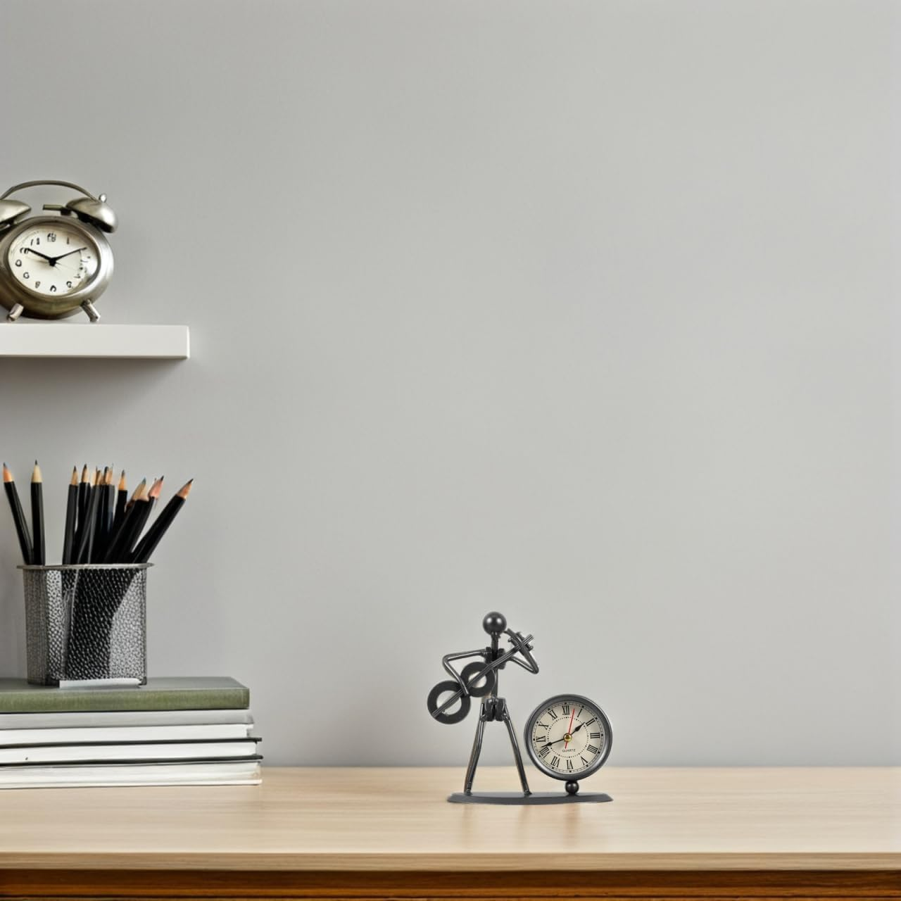 Ein Metallfiguren-Uhrenständer und ein Stiftehalter stehen auf einem Schreibtisch vor einer grauen Wand.