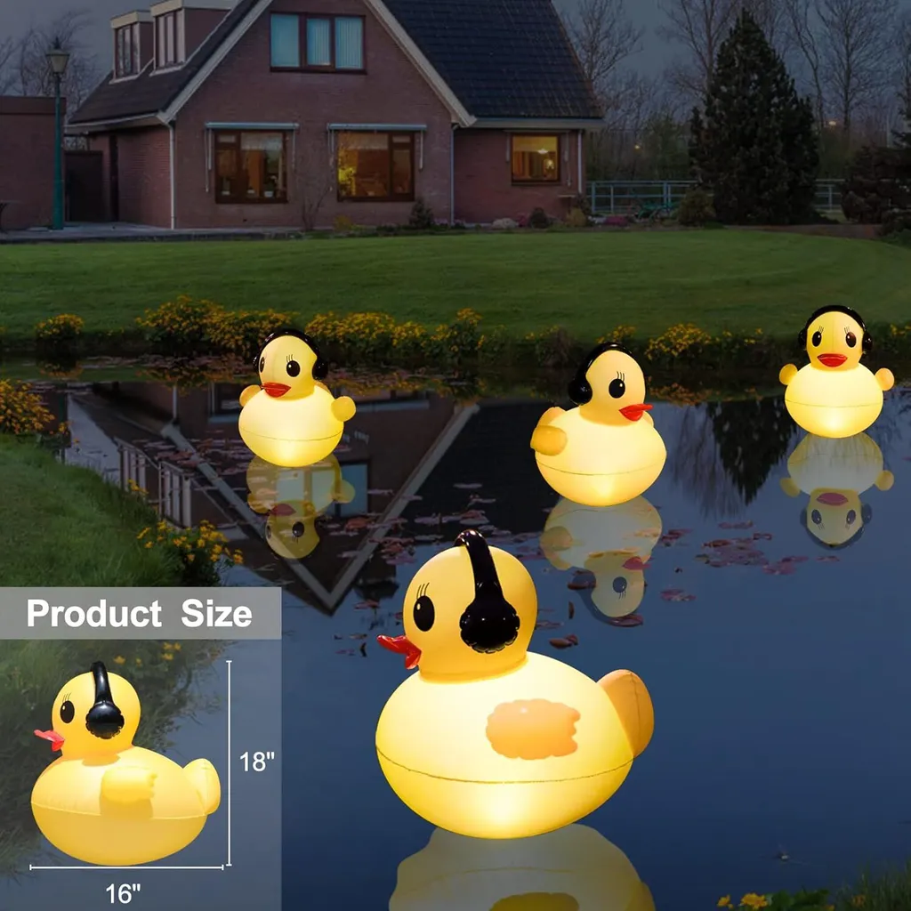 Vier beleuchtete Enten-Teichlichter schwimmen in der Dämmerung in einem Teich, im Hintergrund ein Haus.