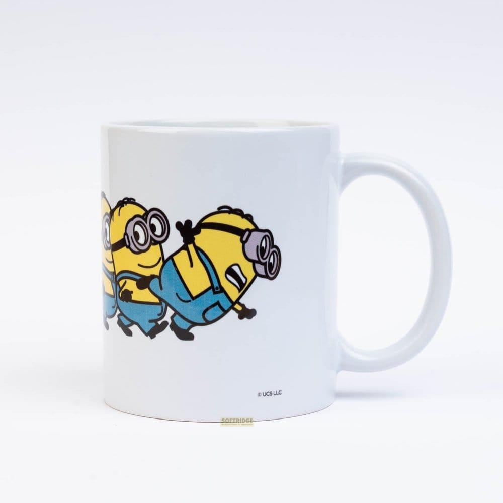 Una taza de cerámica blanca con tres personajes amarillos de Minions con peto azul sobre fondo liso.