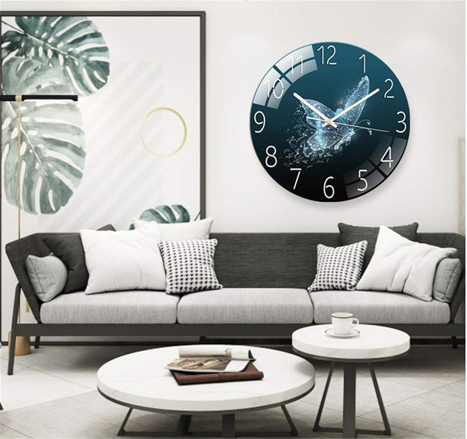 Ein Wohnzimmer mit grauem Sofa, weißen Kissen, runden Couchtischen und einer großen Schmetterlings-Wanduhr.