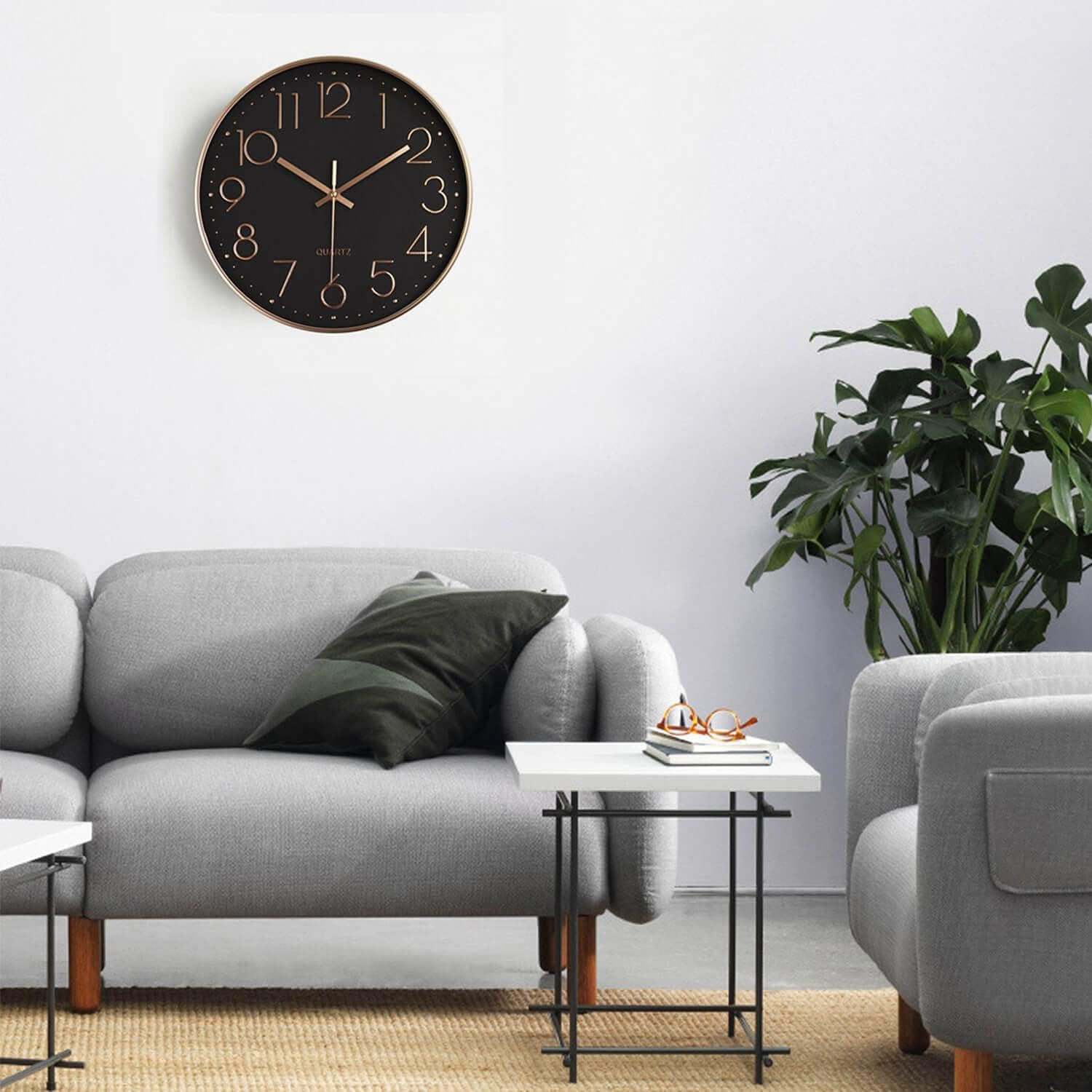 Wohnzimmer mit grauer Couch, runder schwarzer Wanduhr, kleinem Beistelltisch und grüner Topfpflanze.