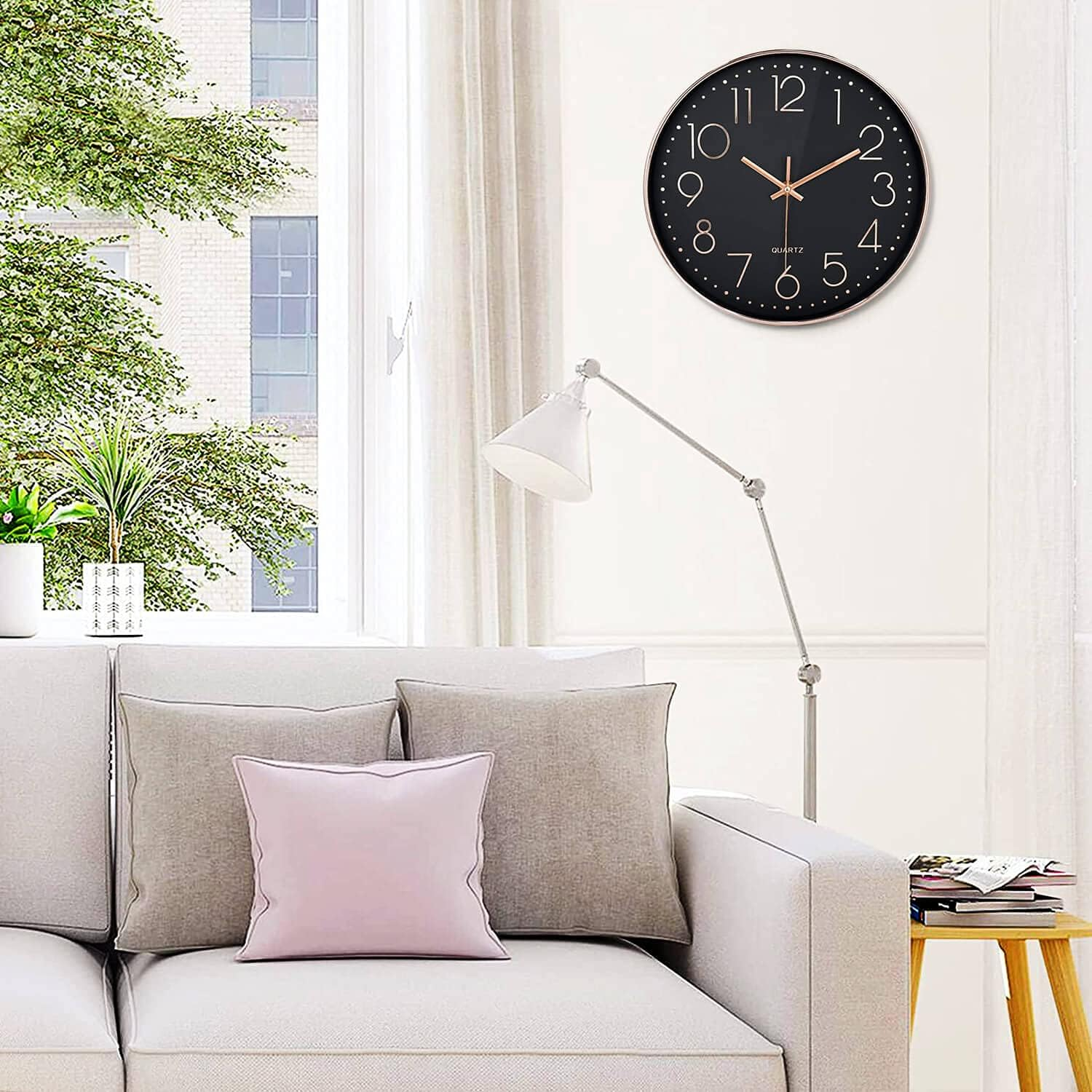 Wohnzimmer mit hellem Sofa, Kissen, moderner Wanduhr, Stehlampe und Fenster mit Blick auf Bäume.