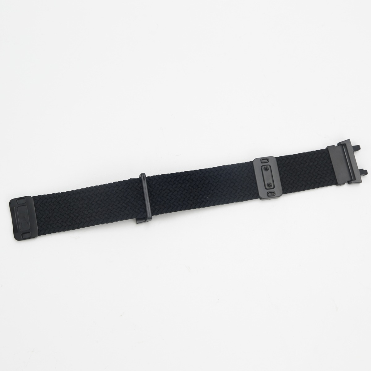 Ein schwarzes gewebtes Uhrenarmband mit schwarzen Metallverschlüssen liegt diagonal auf weißem Hintergrund.