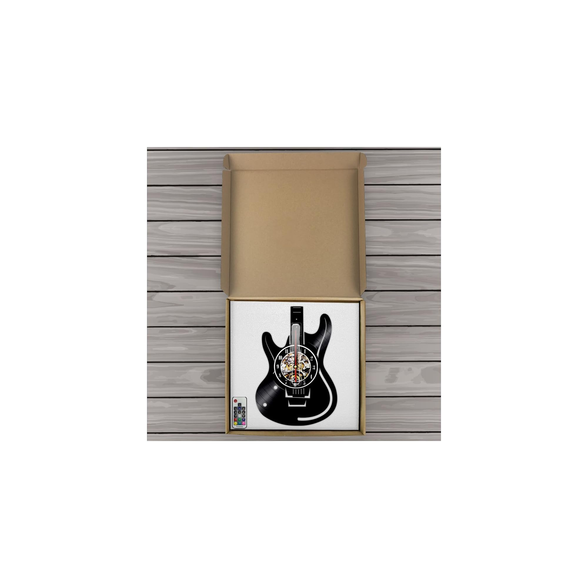 Eine schwarze E-Gitarren-Wanduhr mit Fernbedienung liegt in einer offenen Kartonschachtel auf einem Holztisch.