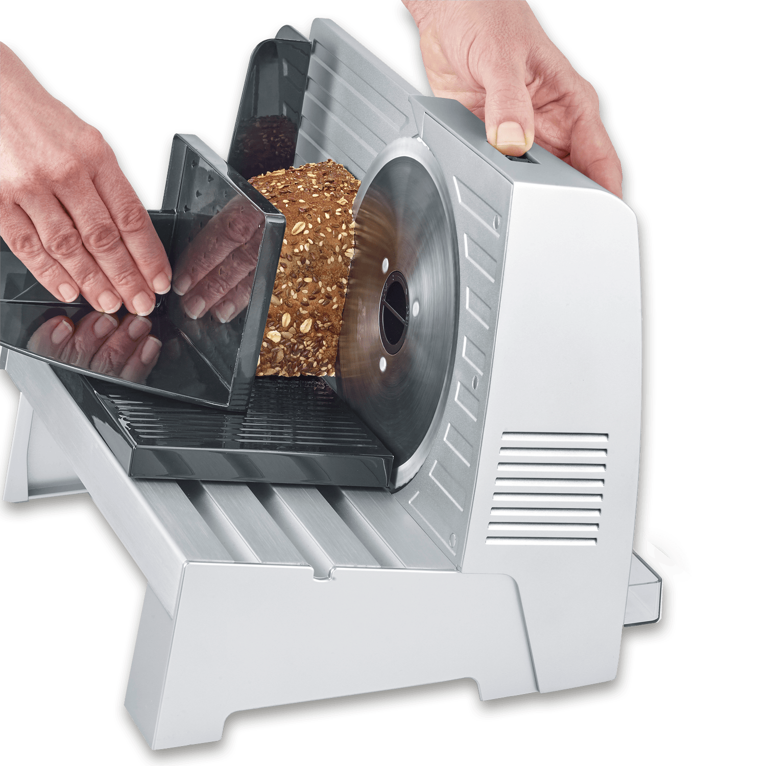 Hände schneiden ein Vollkornbrot mit Körnern auf einer elektrischen Brotschneidemaschine auf schwarzem Hintergrund.