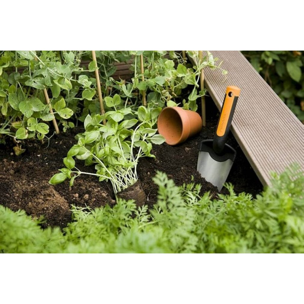Ein Hochbeet mit grünem Gemüse, einer kleinen Pflanze, einem Tontopf und einer Gartenschaufel.