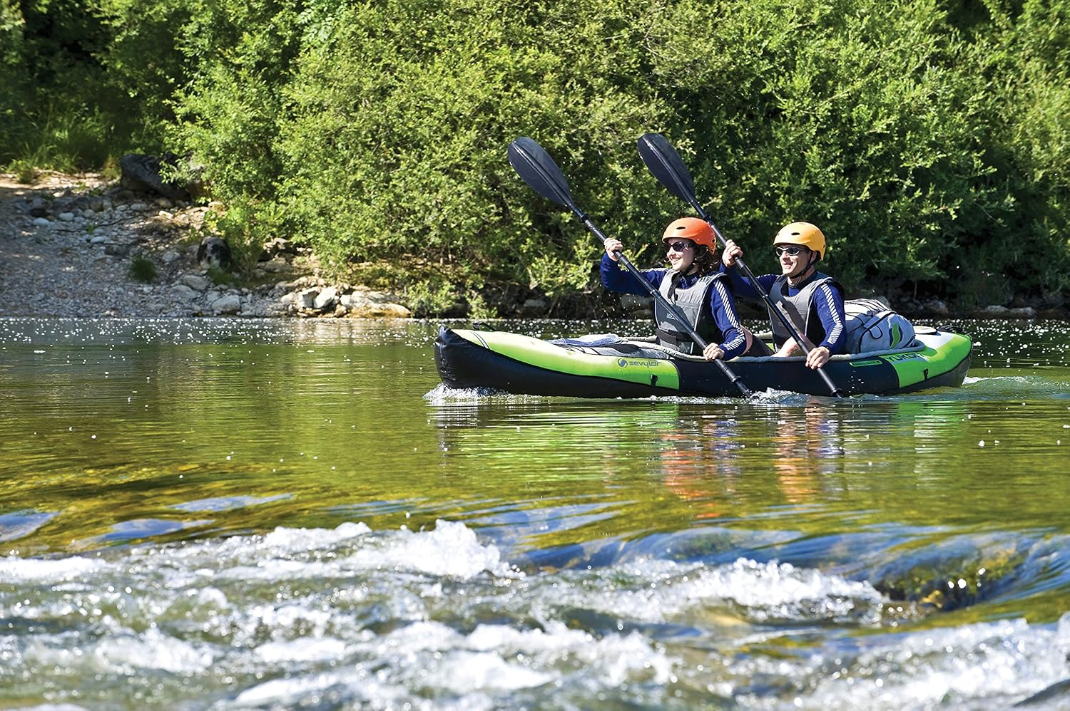 Zwei Personen mit Helmen kajaken auf einem ruhigen, grünen Fluss mit üppigen Bäumen.