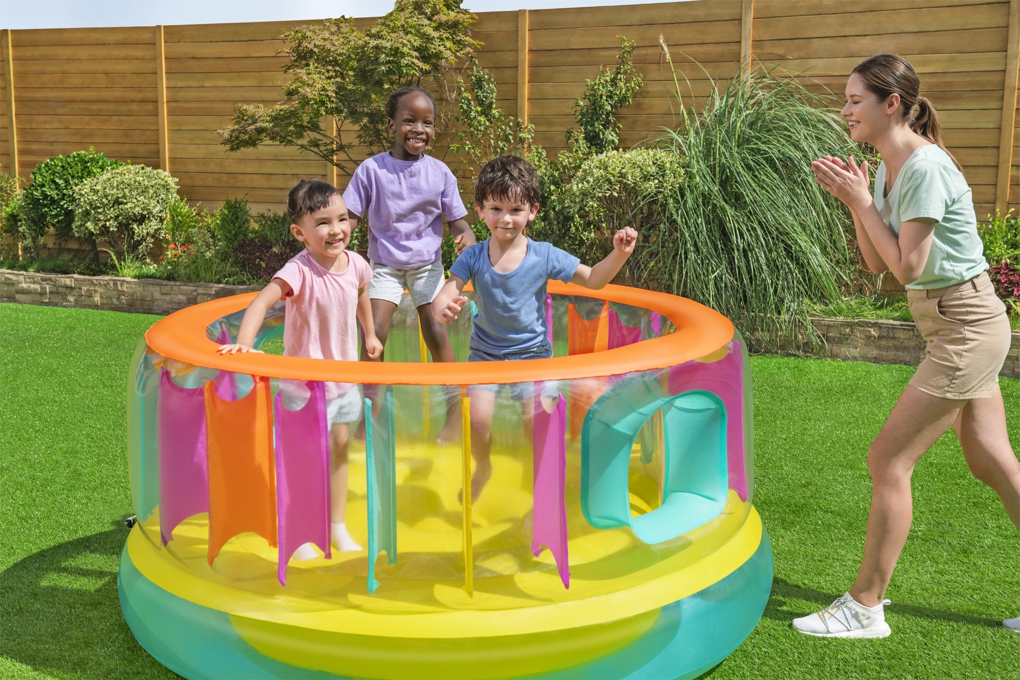 Tre bambini saltano dentro un castello gonfiabile colorato in giardino mentre una donna guarda.