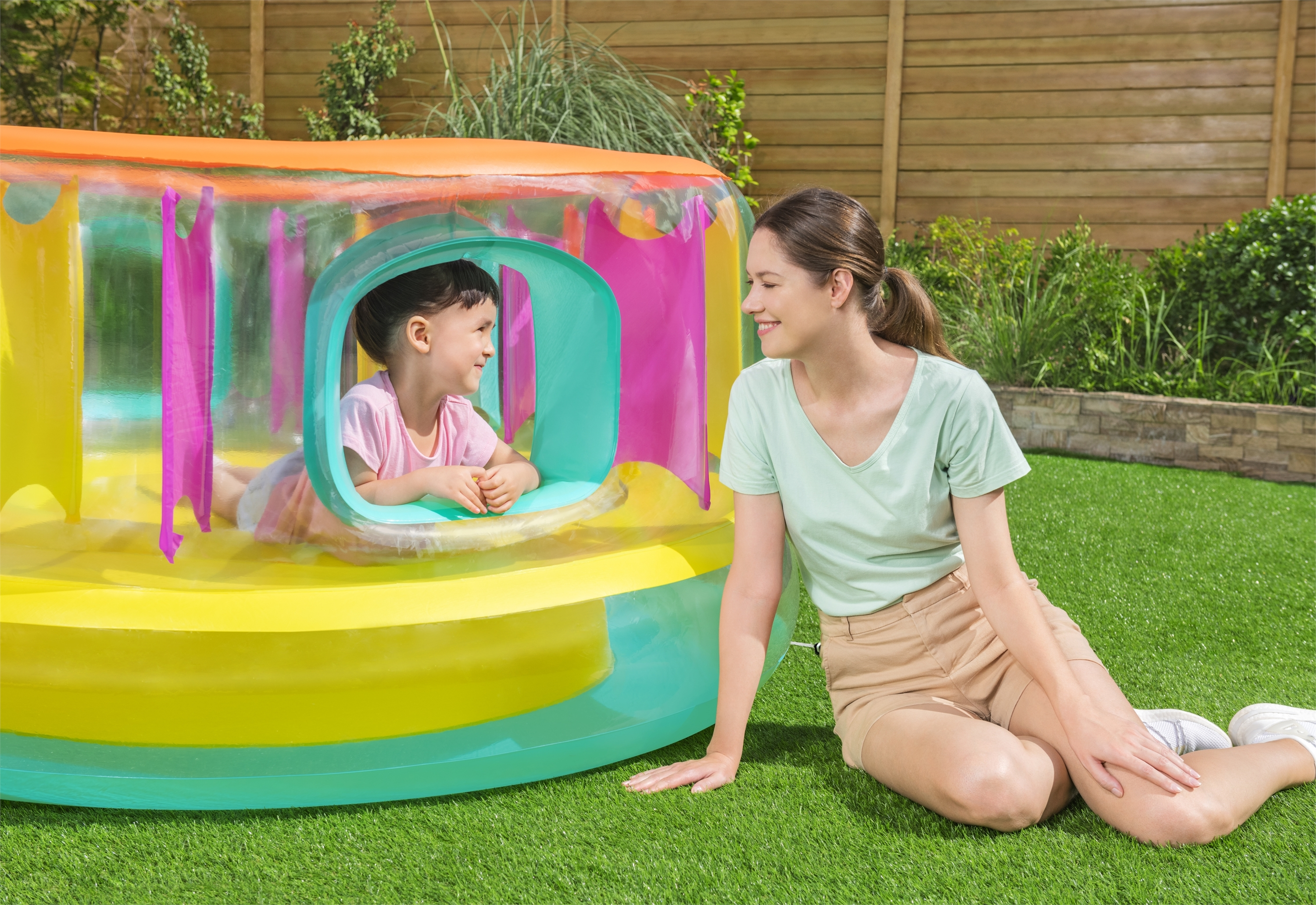Una madre sorride alla sua bambina che guarda fuori da una struttura da gioco gonfiabile e colorata.