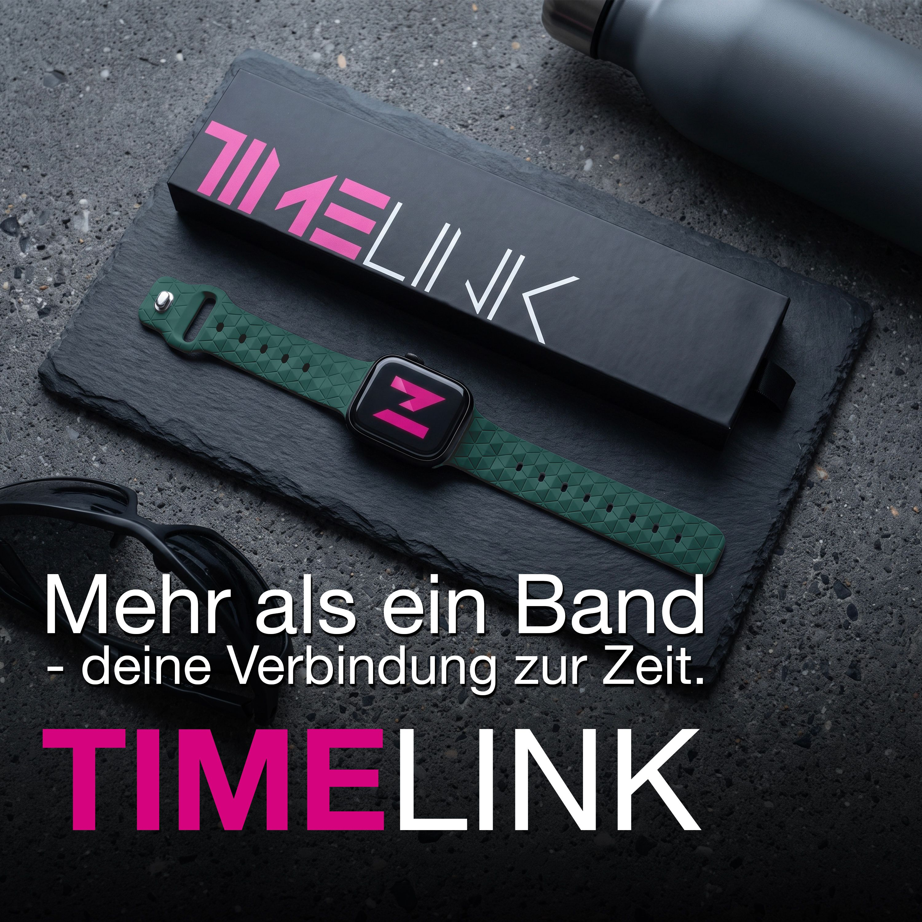 Eine Smartwatch mit grünem Musterarmband, schwarzer Timelink-Box und Sonnenbrille auf dunklem Schiefer.