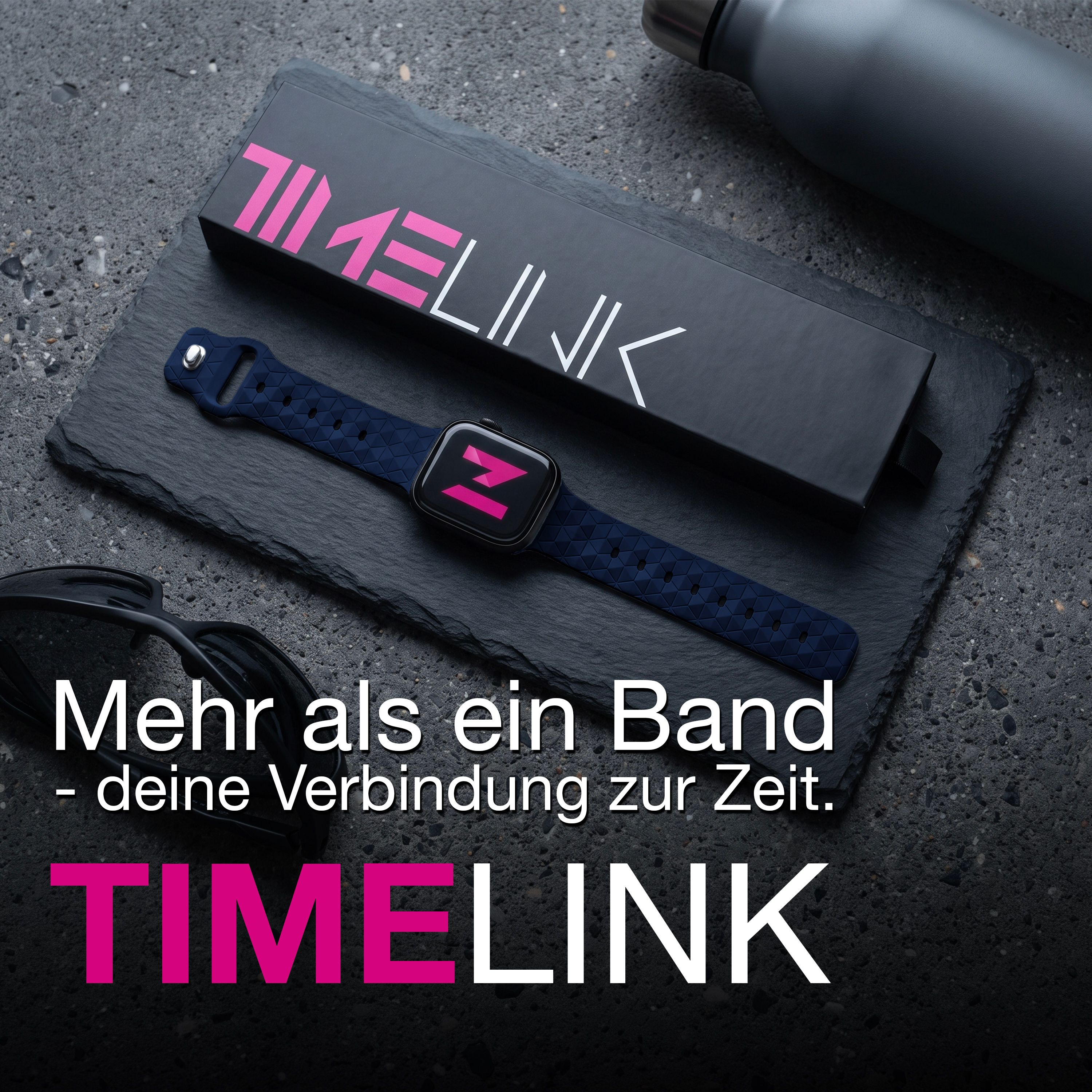Eine Smartwatch mit blauem Musterarmband liegt neben ihrer Timelink-Box, einer Sonnenbrille und Flasche auf Schiefer.