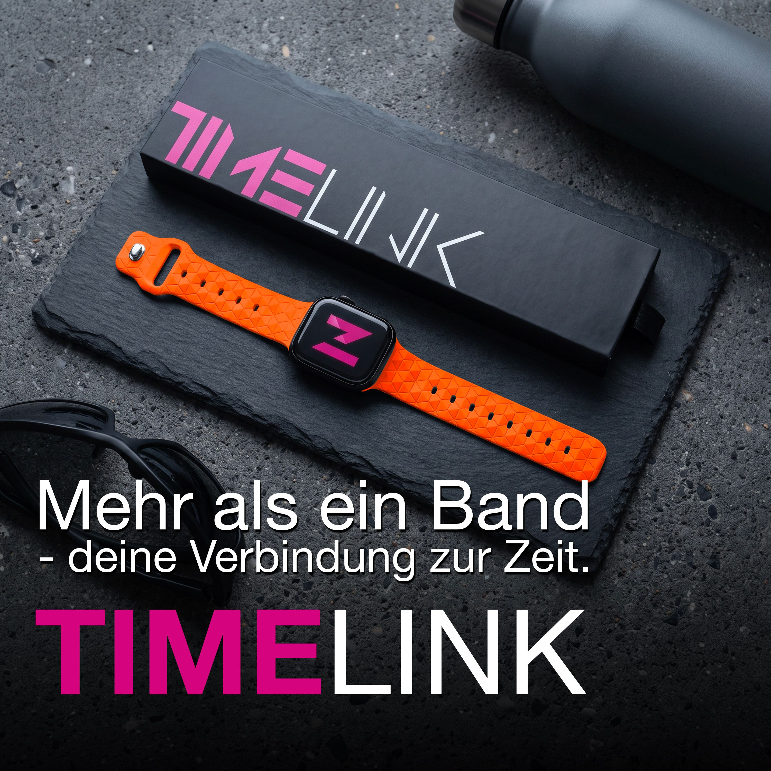 Eine orange Smartwatch mit gemustertem Armband neben einer Box auf schwarzem Stein.