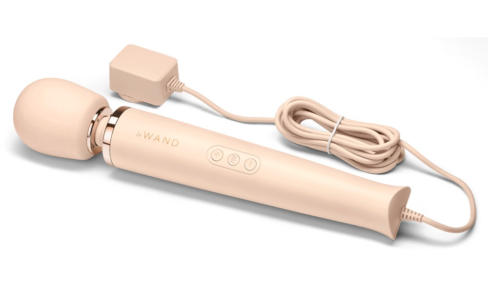Ein pfirsichfarbener Stabvibrator mit Roségold-Akzenten, Bedienelementen und angeschlossenem Netzteil auf weißem Hintergrund.