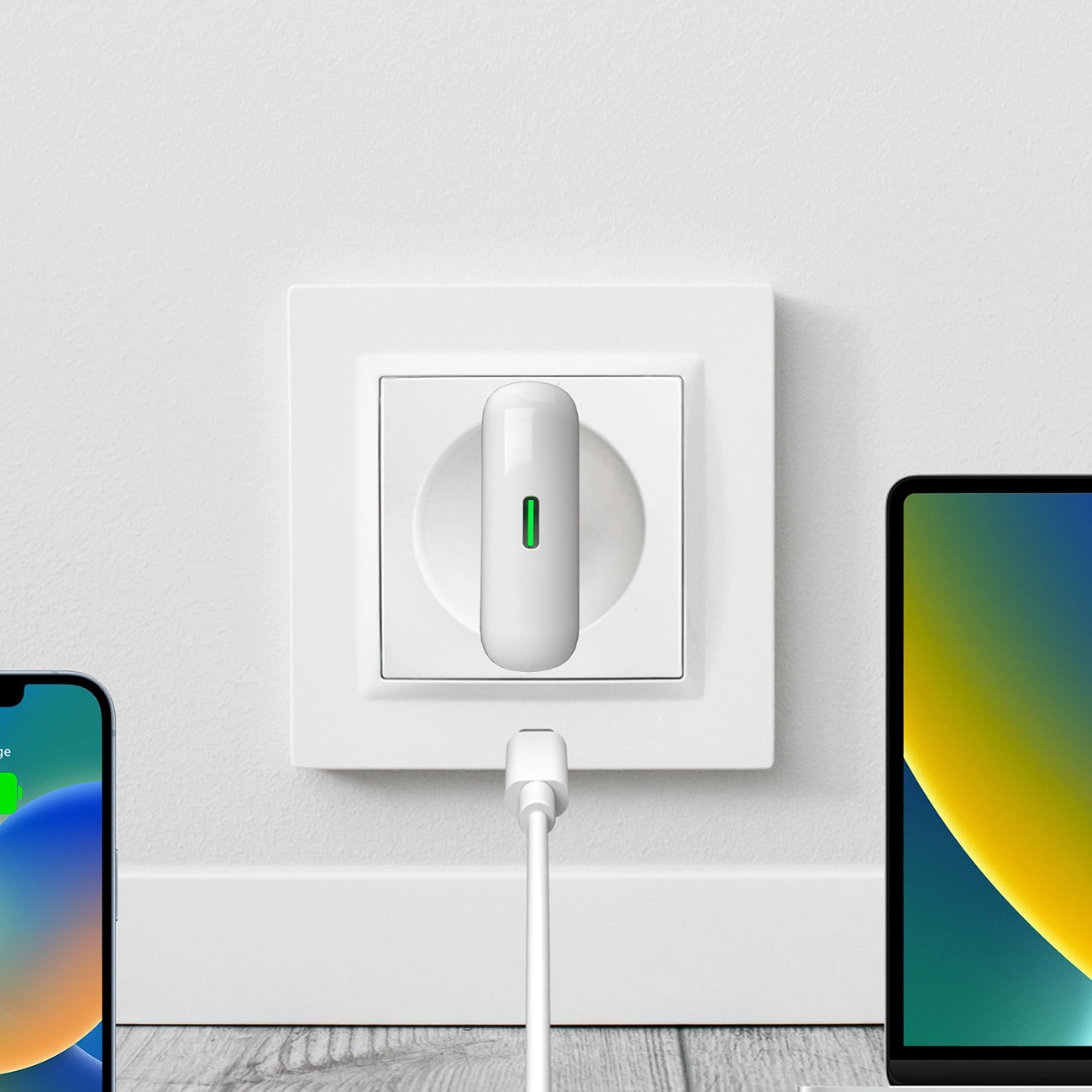 Dispositivo blanco enchufado a la pared con luz verde, flanqueado por un móvil y portátil.
