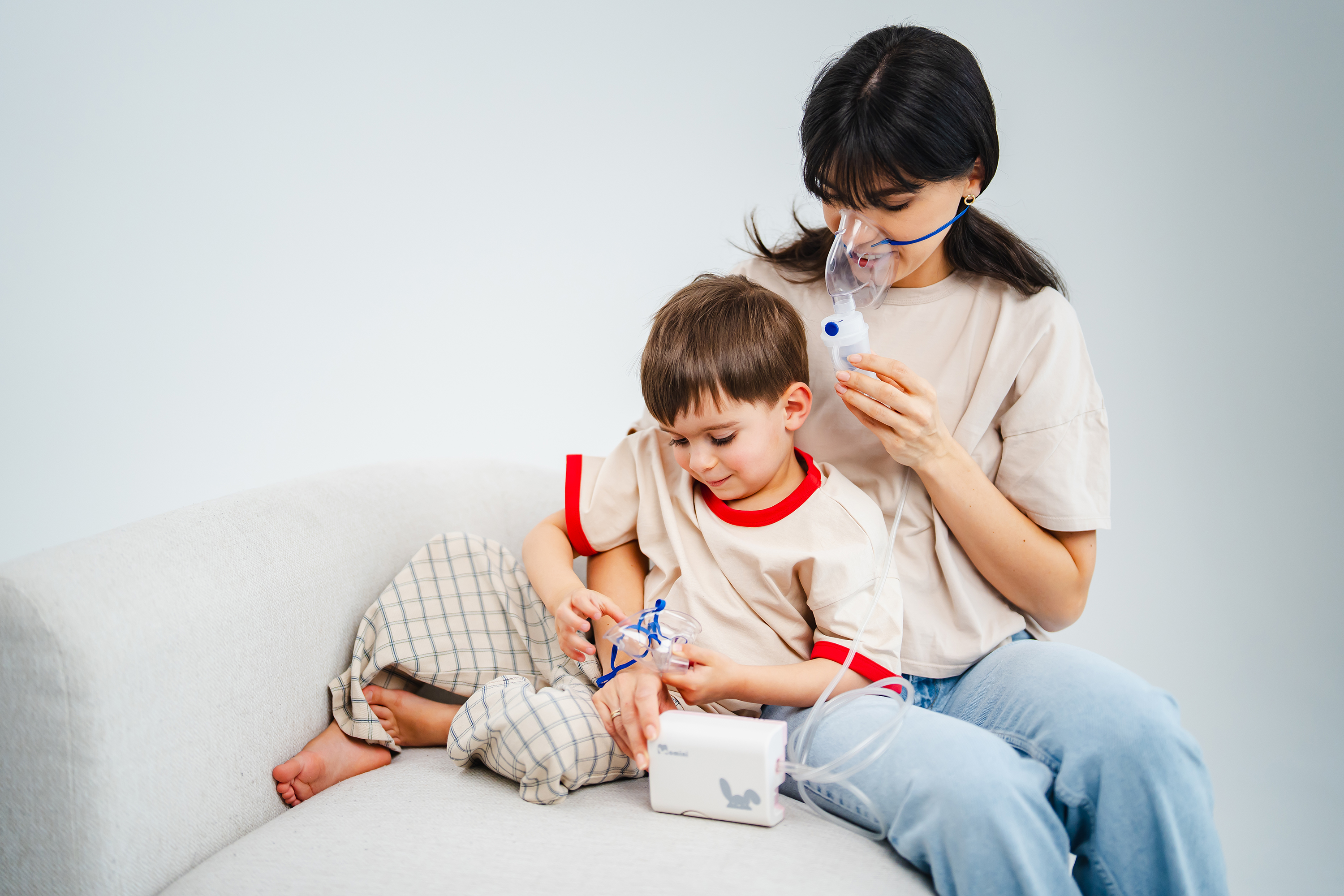 Mutter und Kind sitzen auf einem Sofa und nutzen zusammen ein Inhalationsgerät gegen Husten.