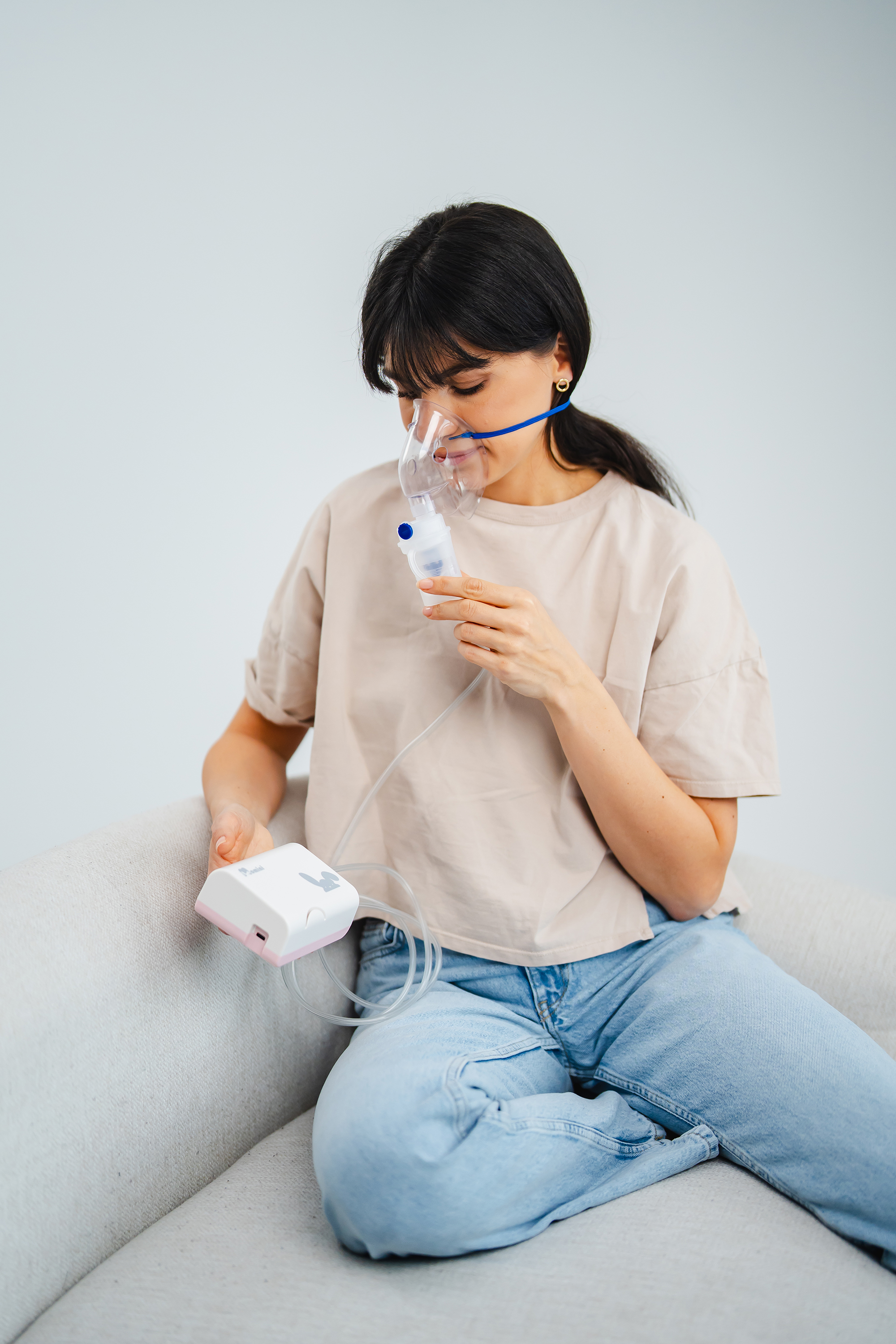 Eine Frau sitzt auf einem Sofa und nutzt einen Inhalator mit Maske.