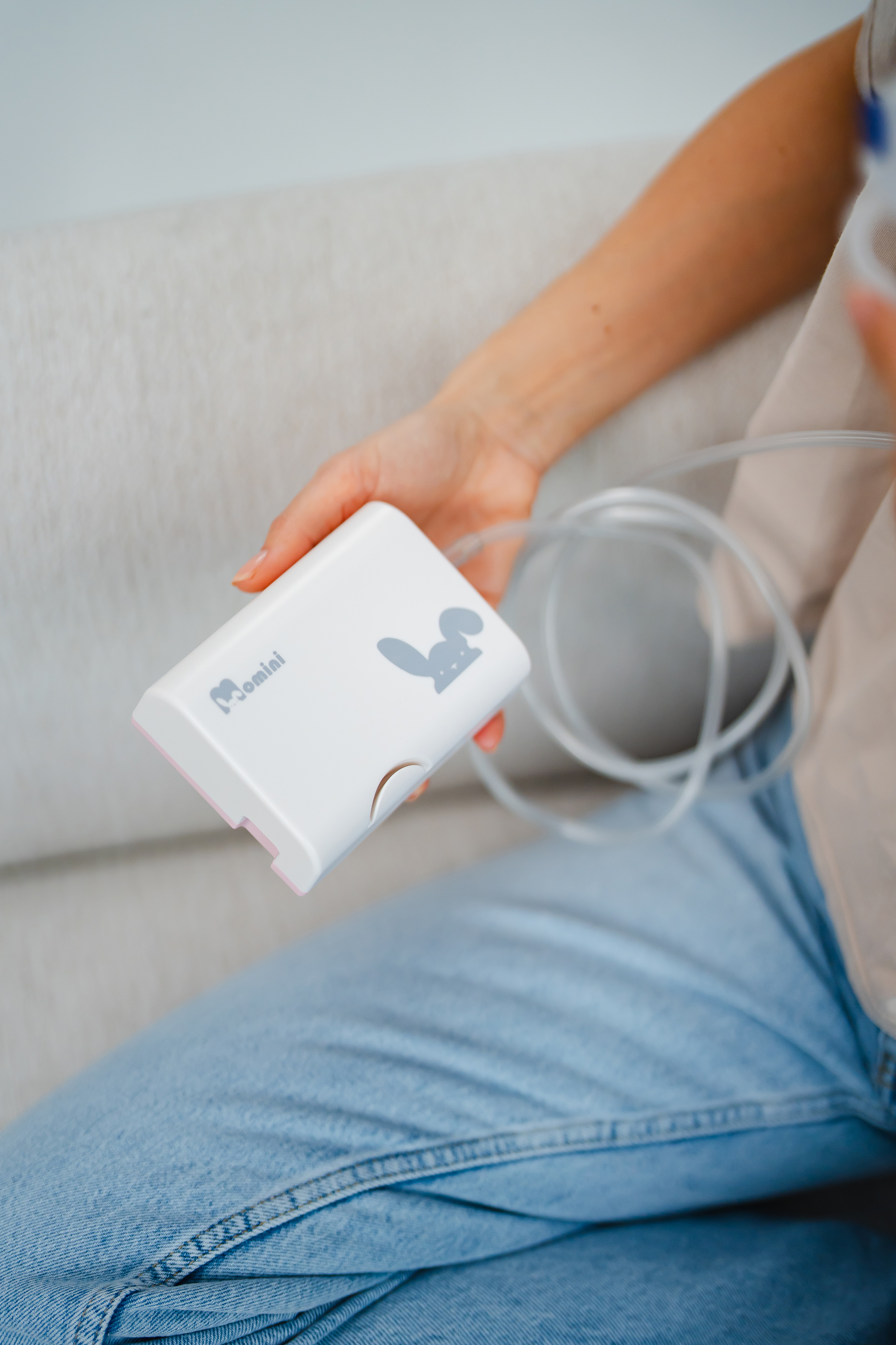 Eine Person hält einen weißen Momini Inhalator mit Hasen-Logo und Schlauch auf einem Sofa.