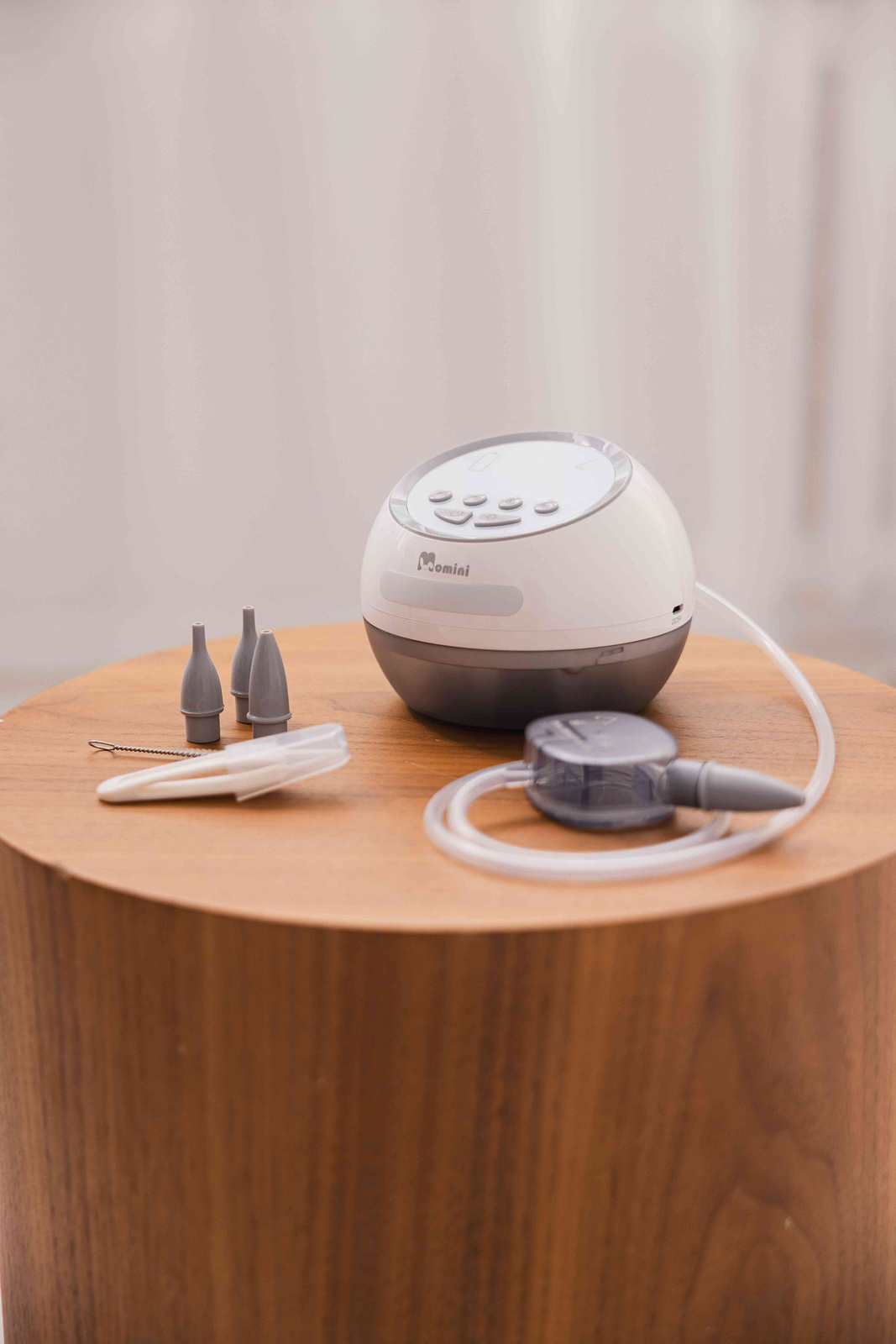 Un aspiratore nasale elettrico bianco e grigio con accessori poggia su un tavolo di legno.