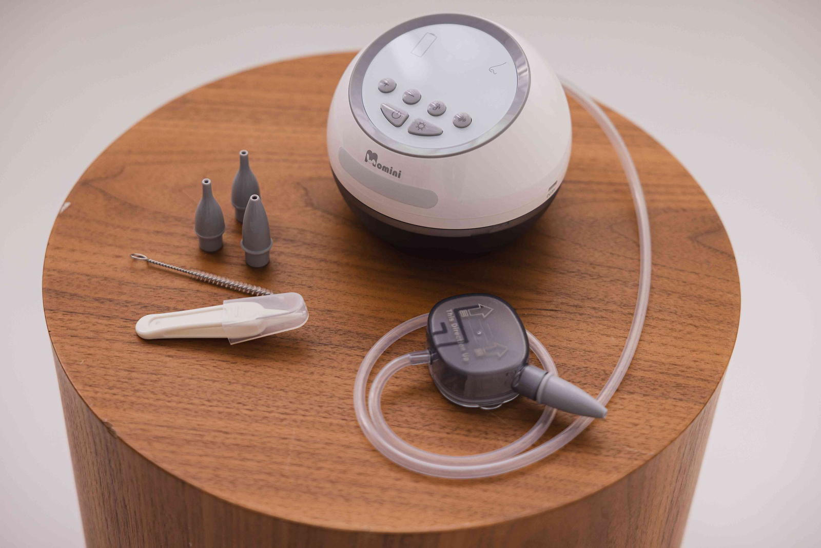 Aspiratore nasale elettrico Momini con punte grigie, spazzola e tubo su superficie in legno.