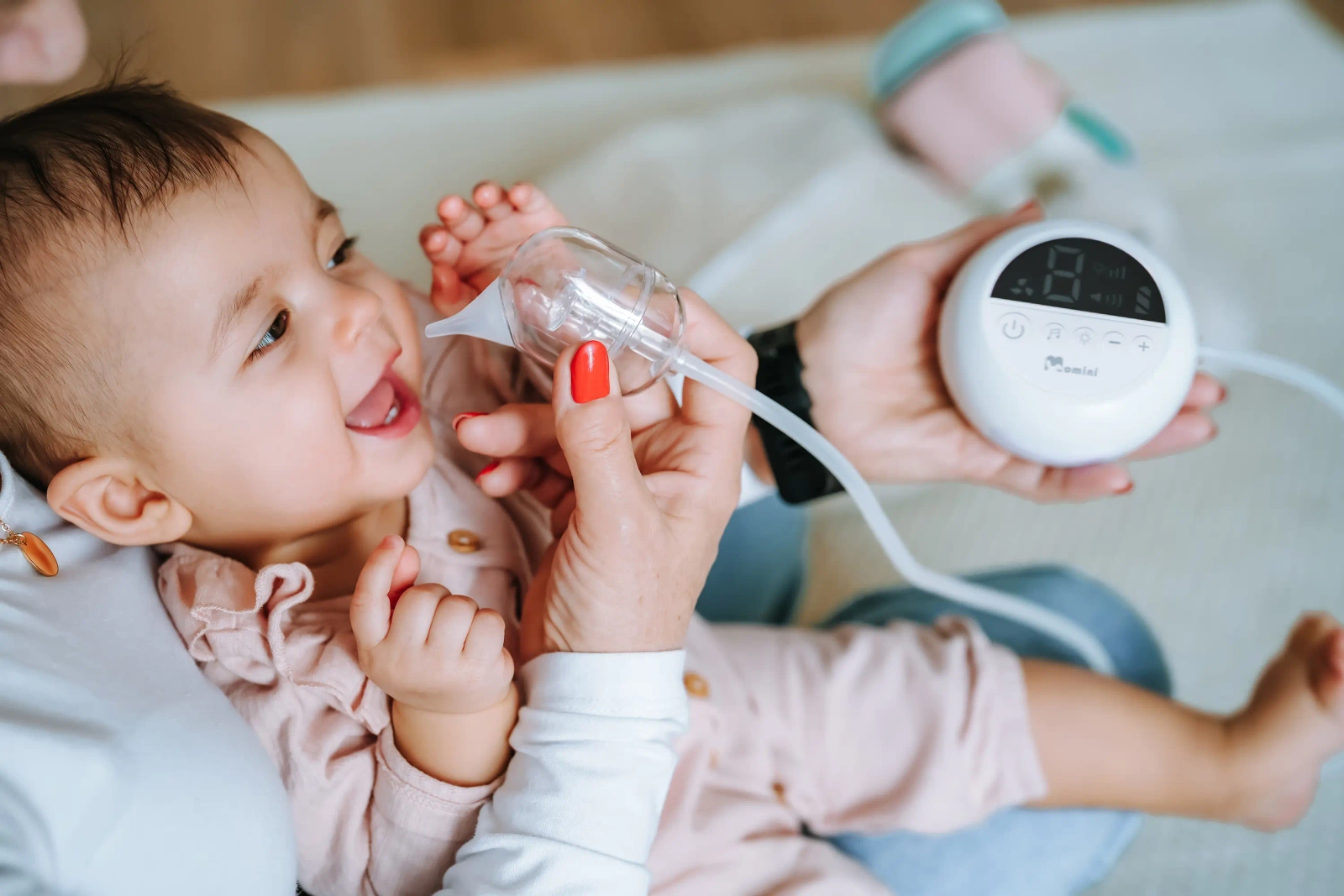 Una madre usa un aspiratore nasale sul suo bambino sorridente.