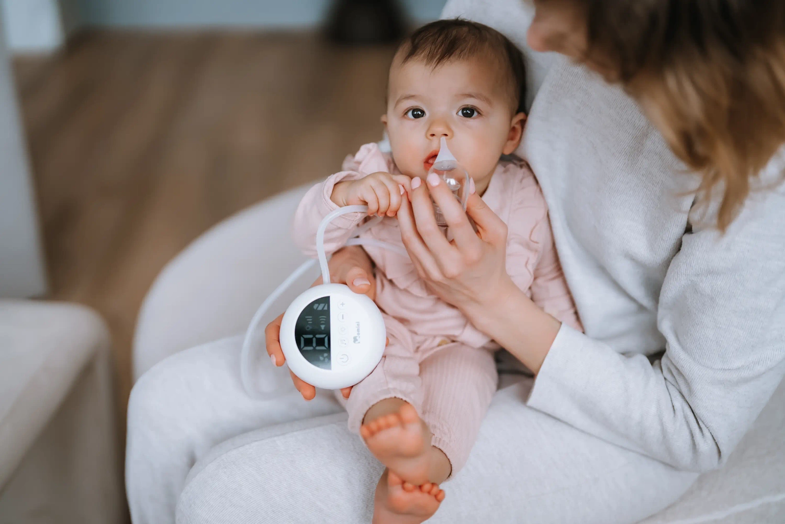 La madre usa un aspiratore nasale sul suo bambino seduto in grembo.