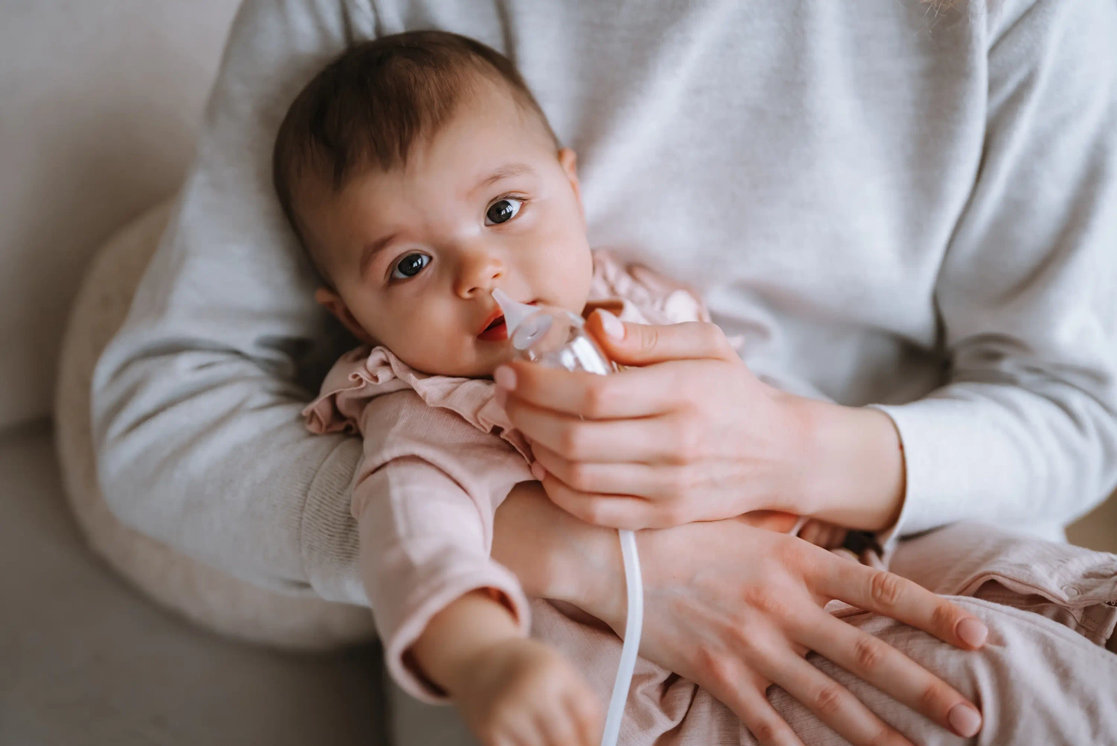 Una madre usa delicatamente un aspiratore nasale sul suo bambino seduto in grembo.