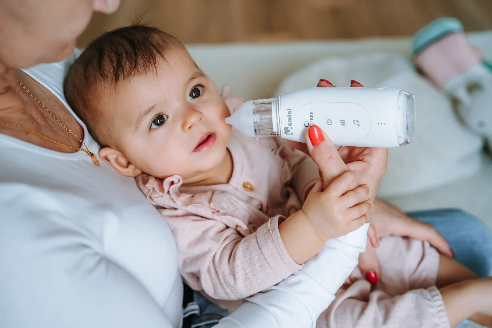 Un bambino viene tenuto in braccio da una persona mentre un aspiratore nasale elettronico gli viene avvicinato al naso.