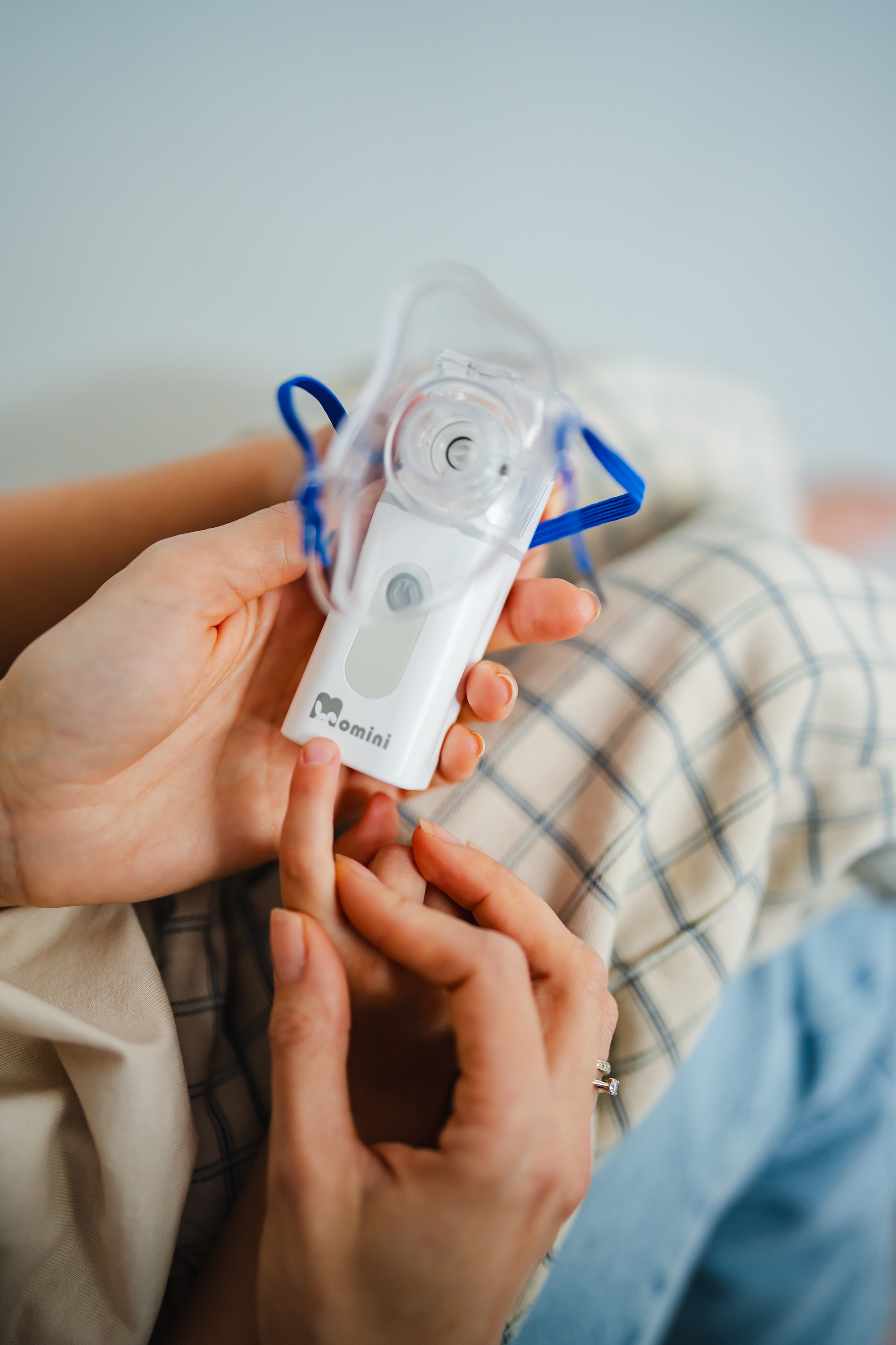 Osoba trzymająca biały nebulizator Omini z przymocowaną przezroczystą maską i niebieską gumką.