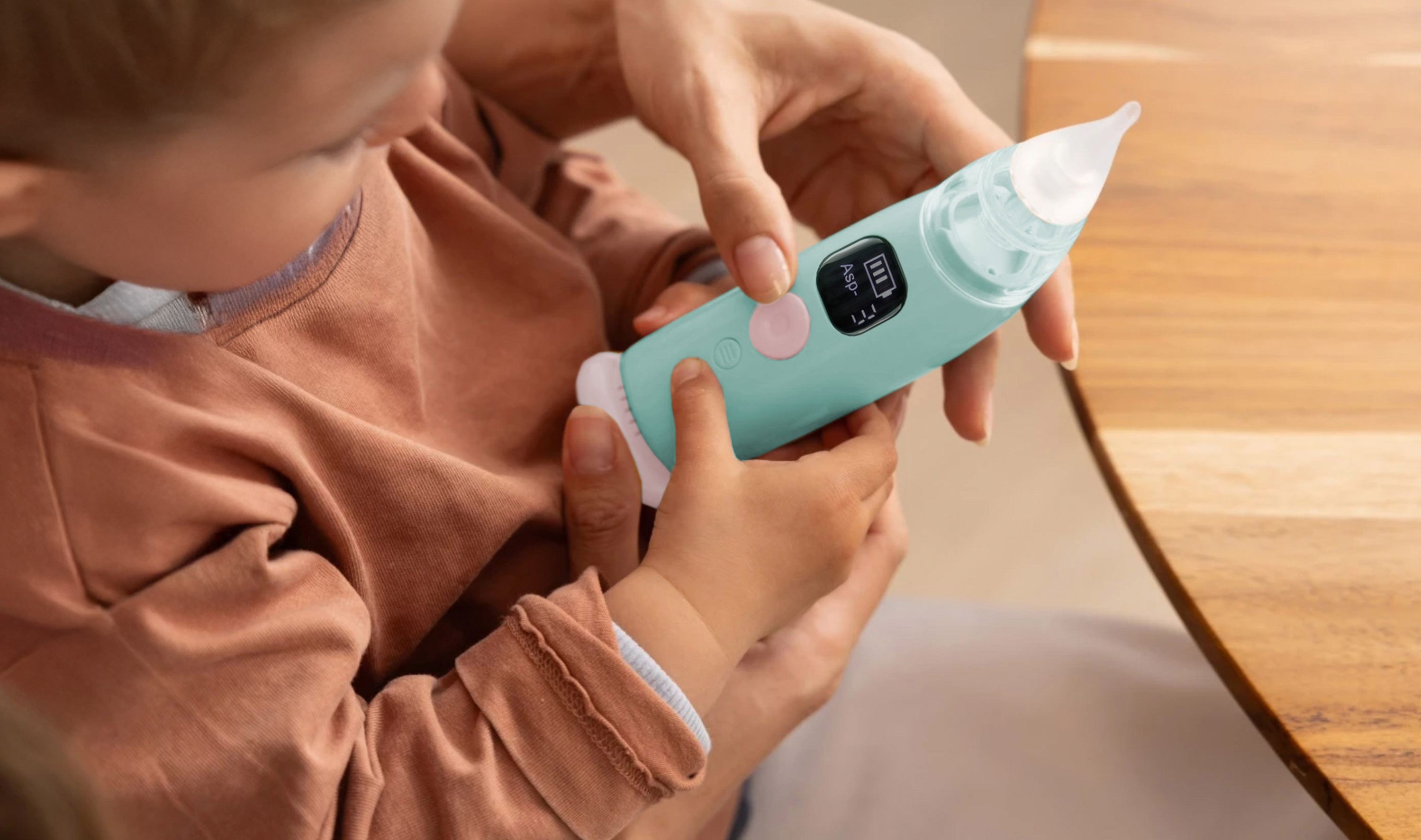 Una mano tiene un aspiratore nasale turchese con schermo digitale mentre un bambino lo tocca.