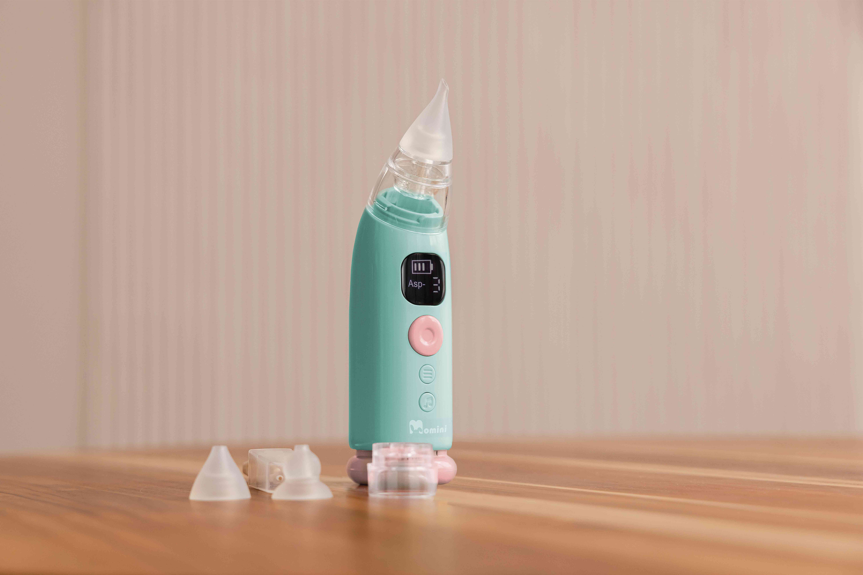 Un aspiratore nasale elettrico turchese e rosa si trova in piedi su un tavolo di legno con punte in silicone.