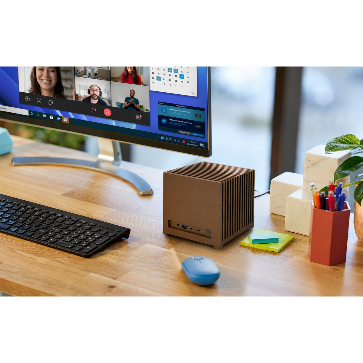 Scrivania in legno con monitor, tastiera, mouse blu, mini PC marrone, note adesive, penne e pianta in vaso.