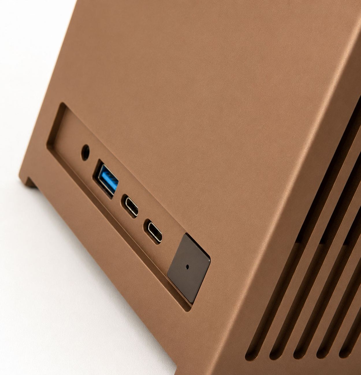 Dispositivo elettronico marrone con porte per cuffie, USB, USB-C e un pulsante quadrato nero su sfondo bianco.