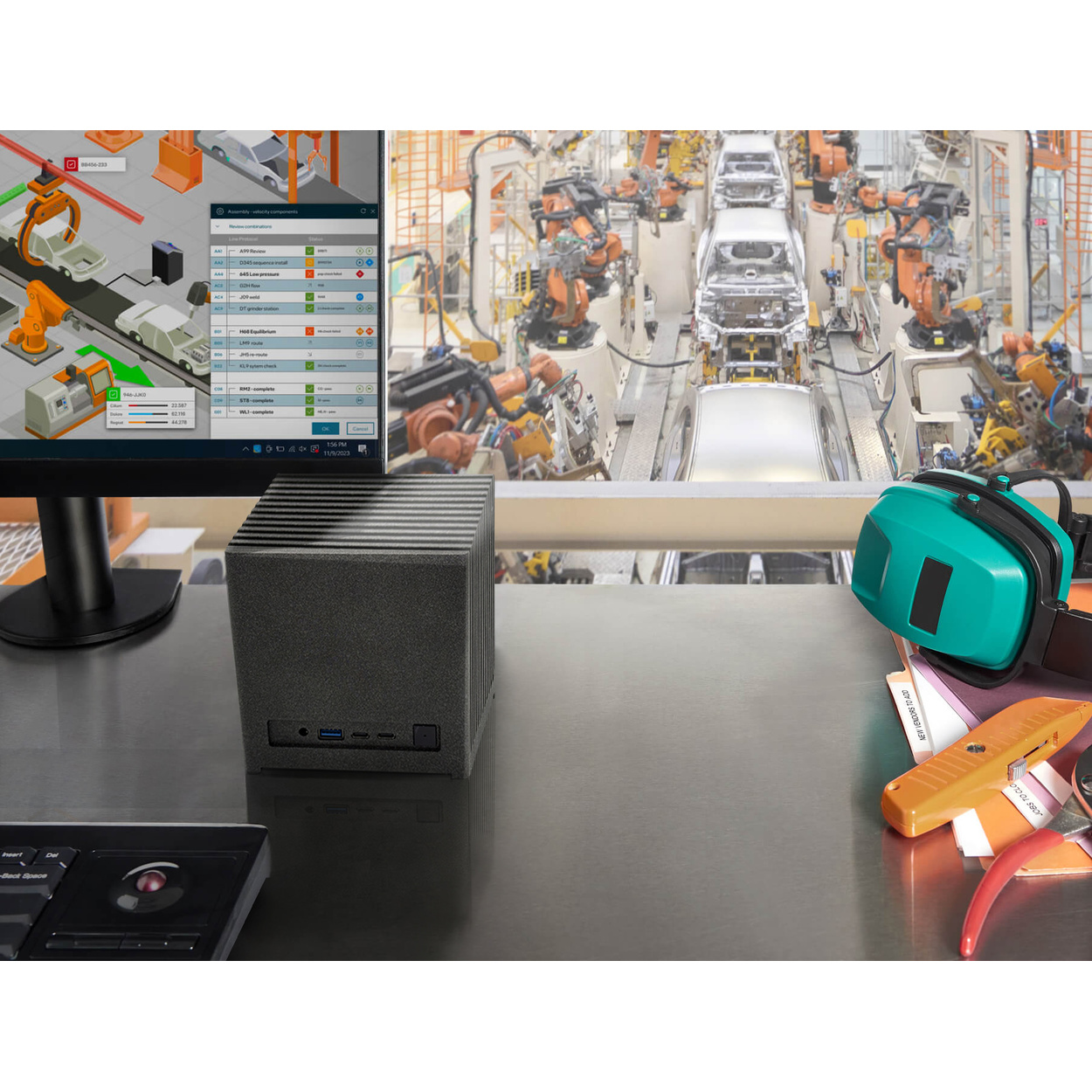 Un mini PC nero su una scrivania con monitor che mostra dati di fabbrica, con vista su una linea di montaggio con robot.