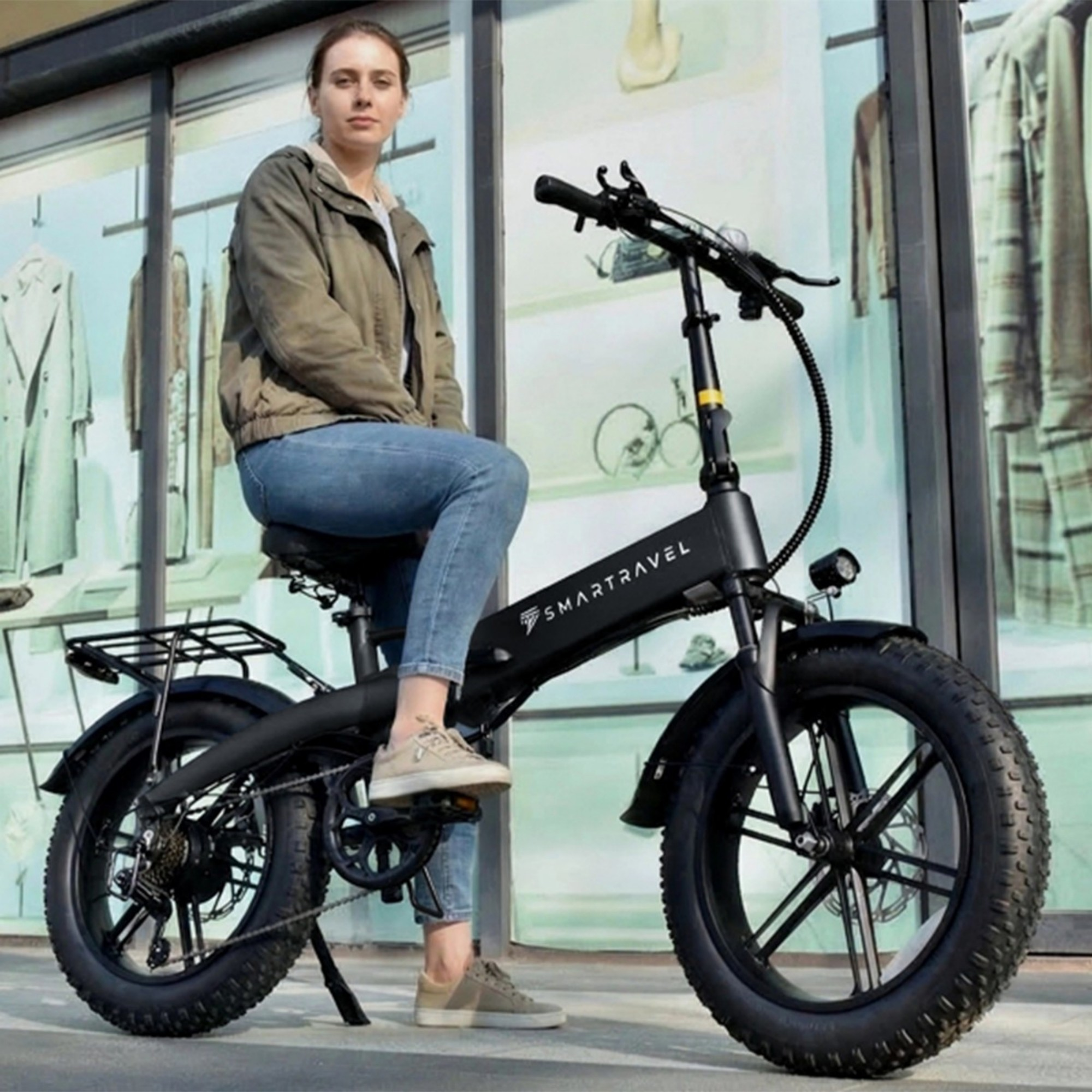 Kobieta siedzi na czarnym rowerze elektrycznym przed witryną sklepowa z odzieżą.