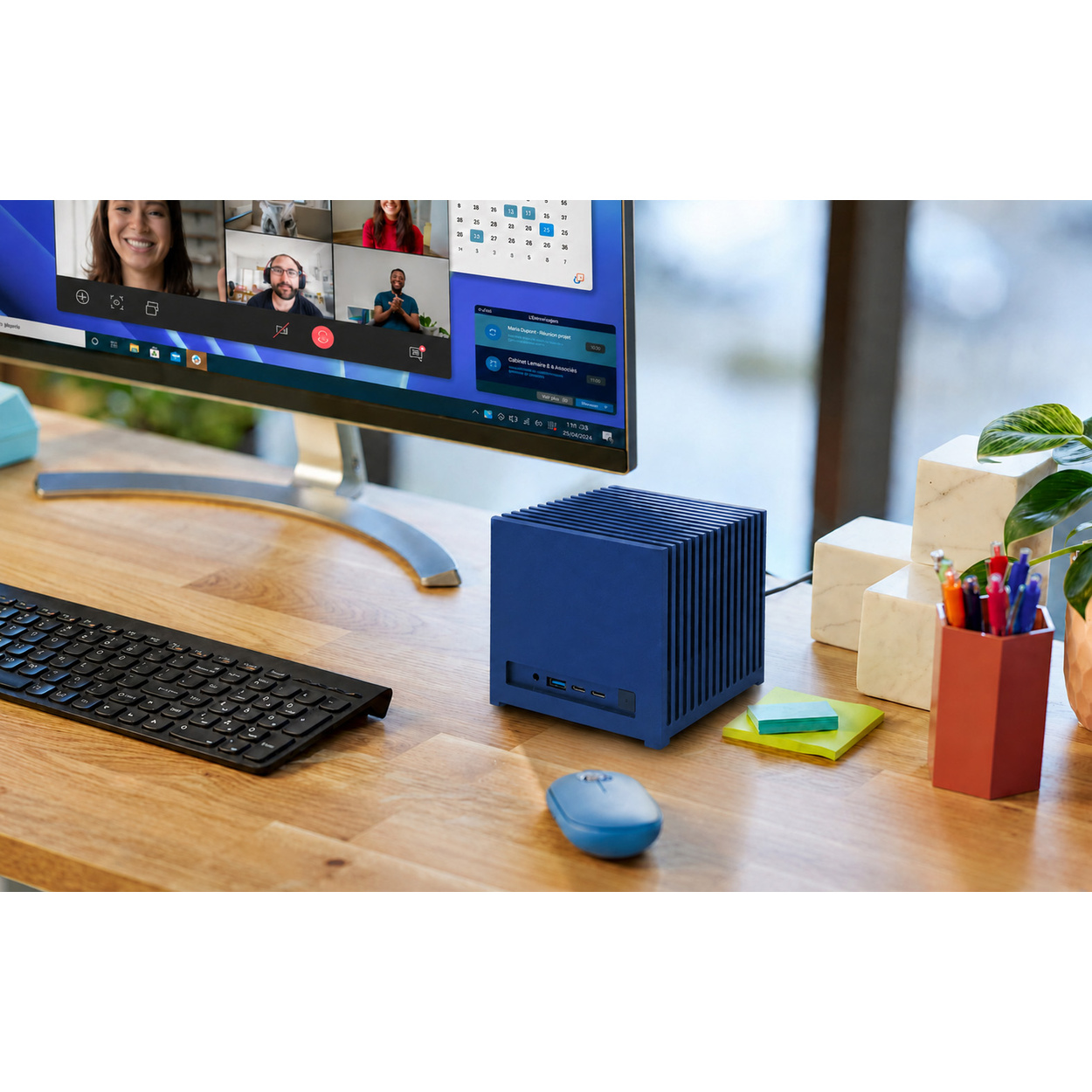 Scrivania con monitor, case PC blu, tastiera, mouse, note adesive e portapenne.