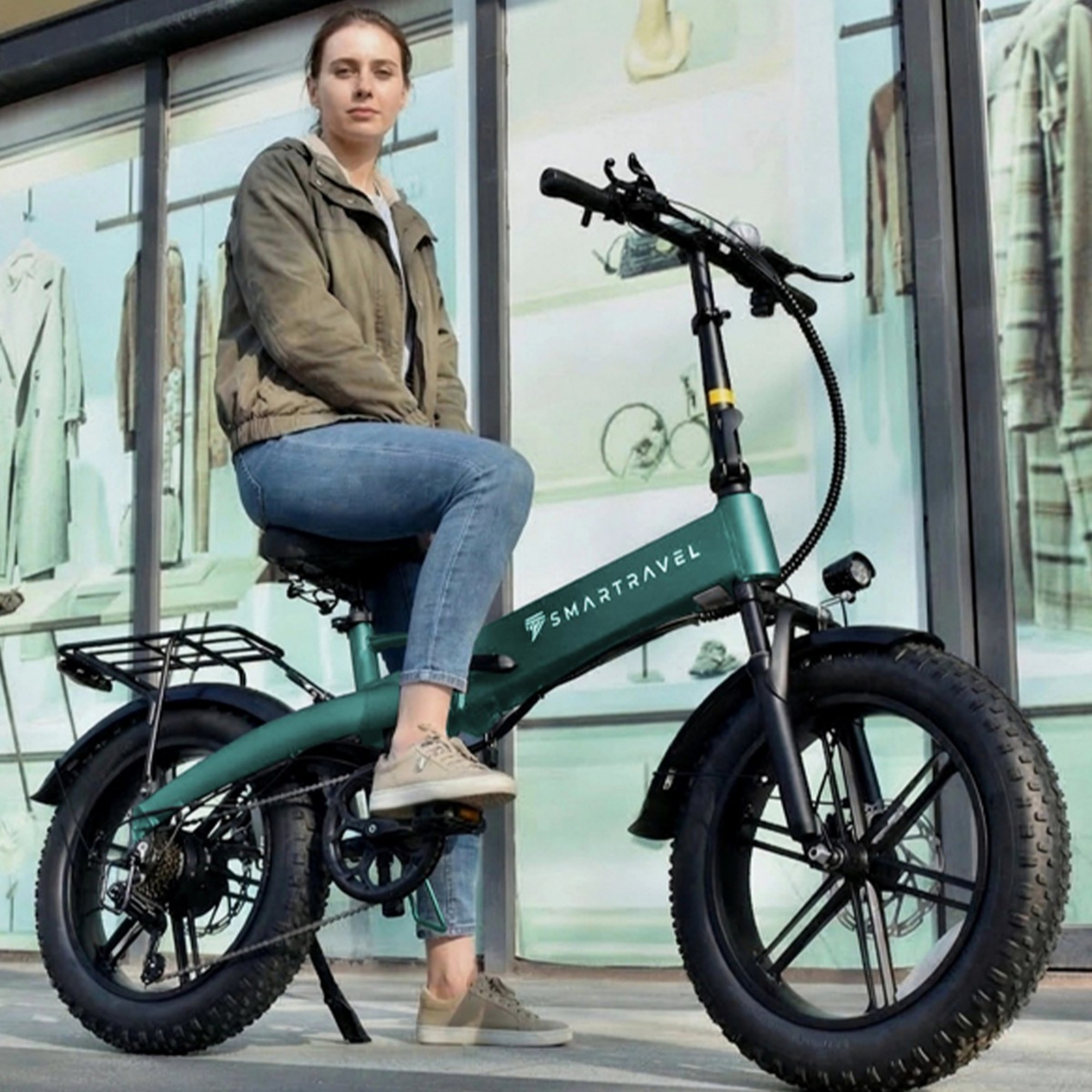 Kobieta siedzi na zielonym rowerze elektrycznym z grubymi oponami przed witryną sklepową.