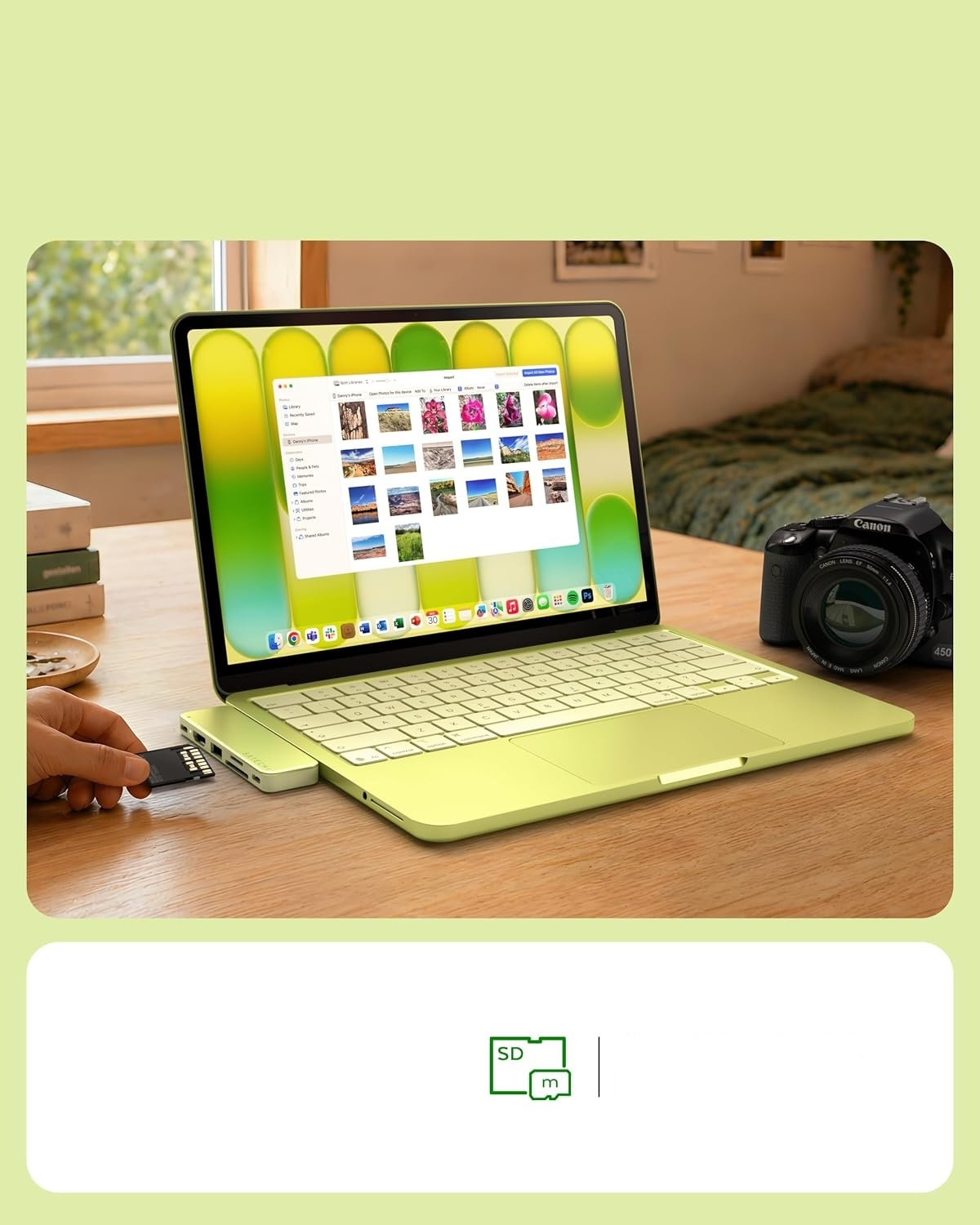 Żółty laptop na drewnianym stole, ręka wsadza kartę SD, obok leży aparat.