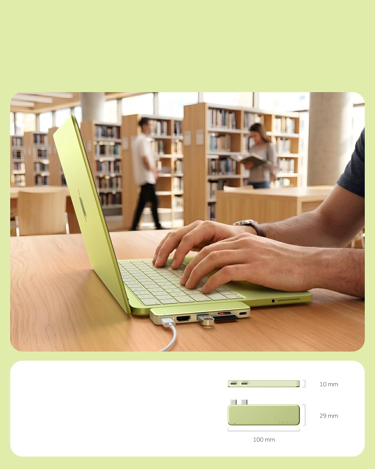 Osoba pisze na zielonym laptopie w bibliotece, z hubem USB podłączonym z boku i wymiarami poniżej.