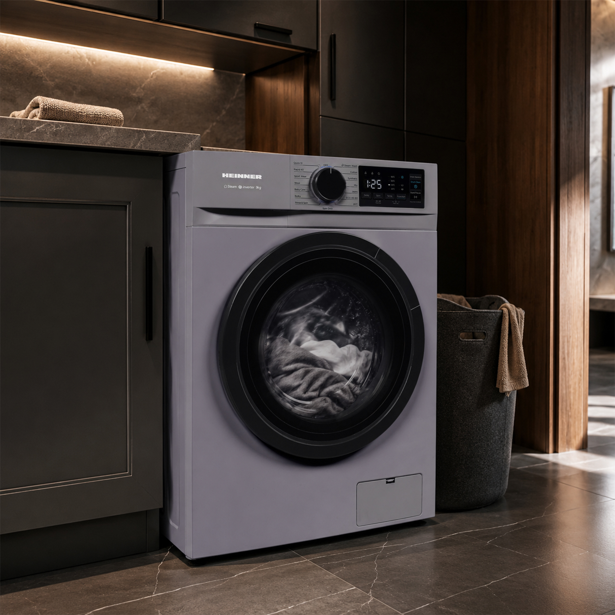 Un lave-linge gris Heinner se trouve dans une cuisine moderne avec des placards sombres et un panier à linge.