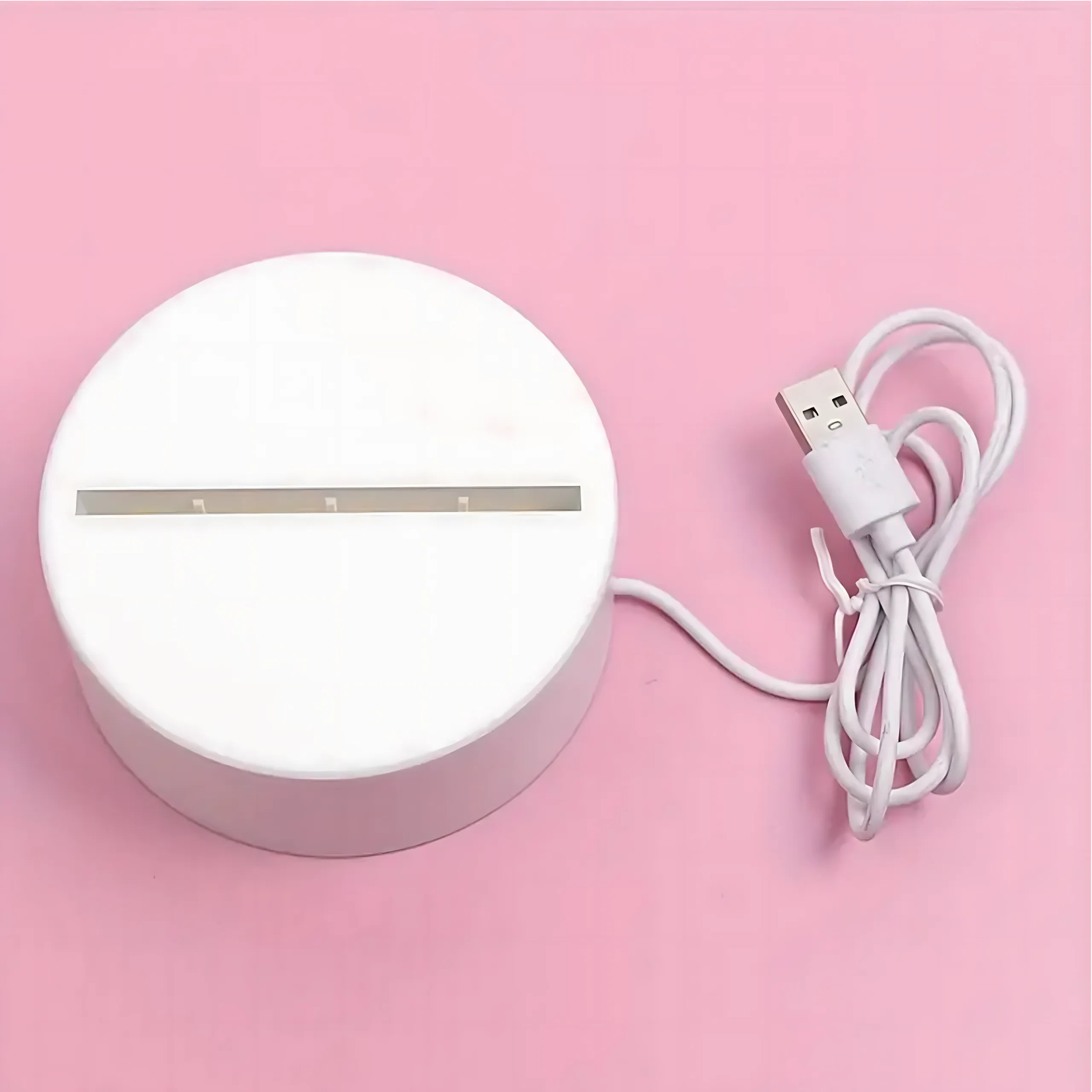 Biała, okrągła akrylowa podstawa lampy z poziomym slotem i dołączonym białym kablem USB na różowym tle.