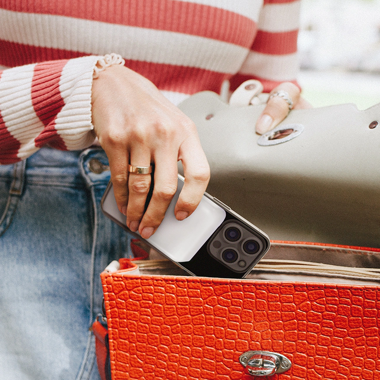 Una donna con un maglione a righe rosse e bianche ripone uno smartphone con power bank in una borsa arancione.