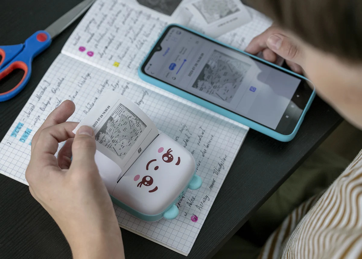 Un bambino usa uno smartphone e una simpatica mini stampante per stampare foto su un taccuino.
