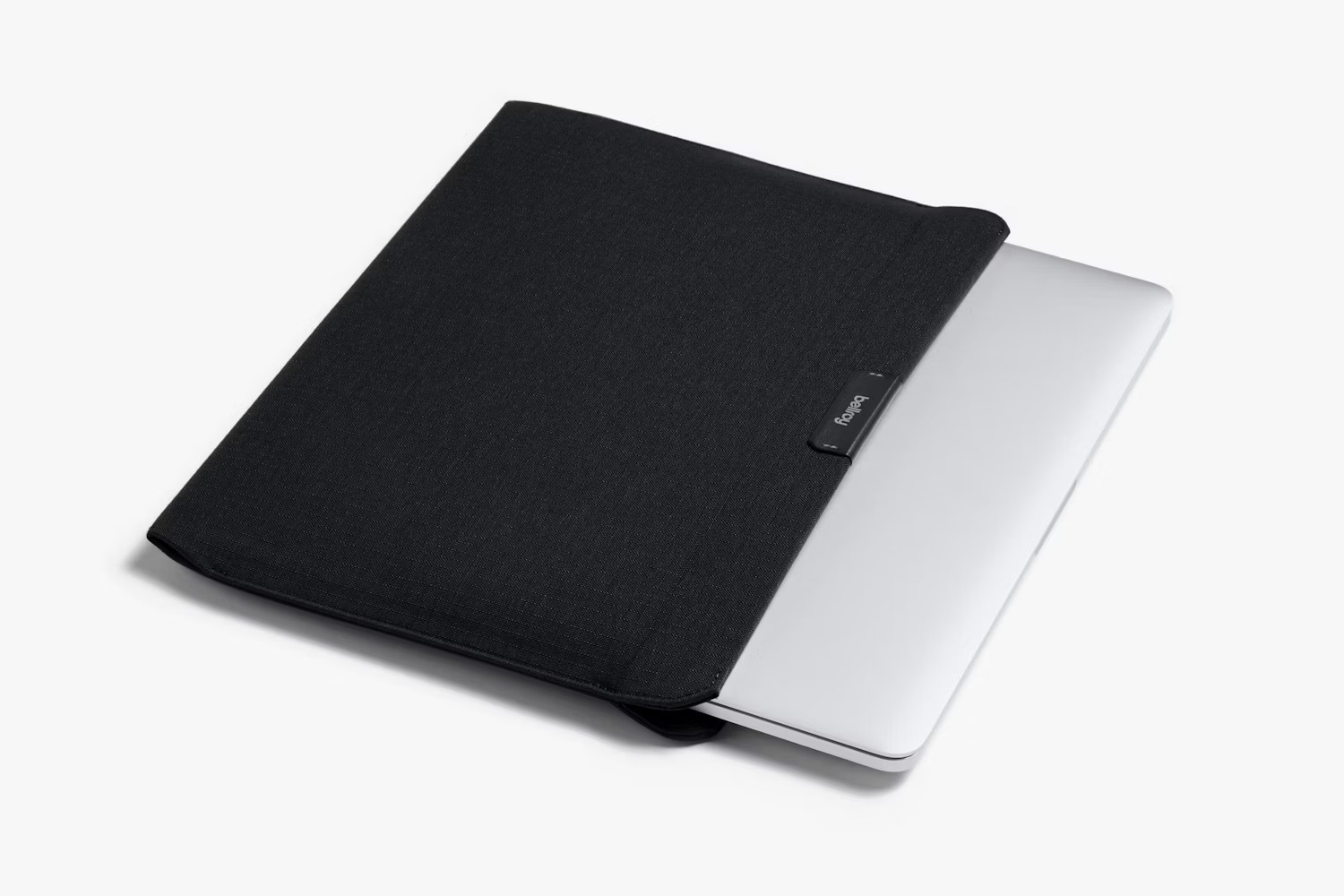 Srebrny laptop w czarnym materiałowym pokrowcu na jasnym tle.