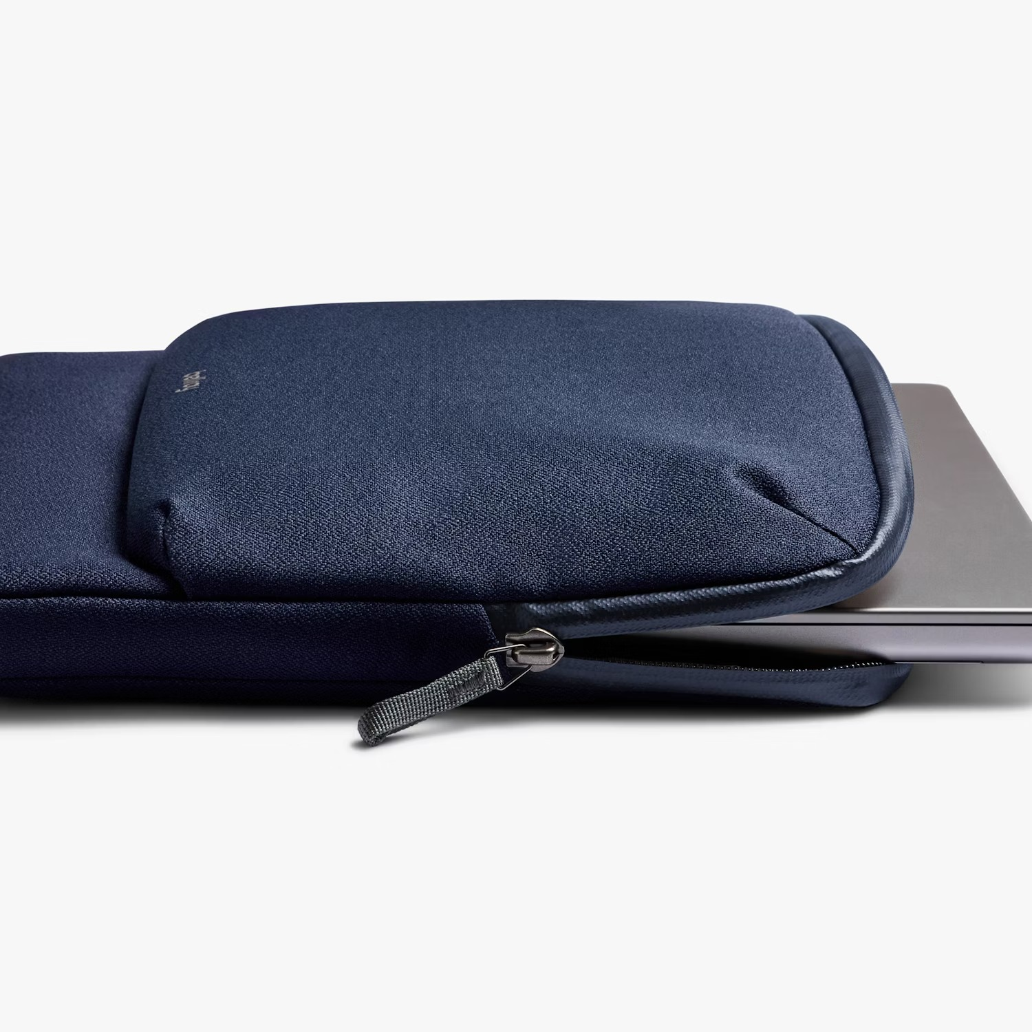 Ciemnoniebieskie etui na laptopa z częściowo otwartym zamkiem i widocznym srebrnym laptopem.