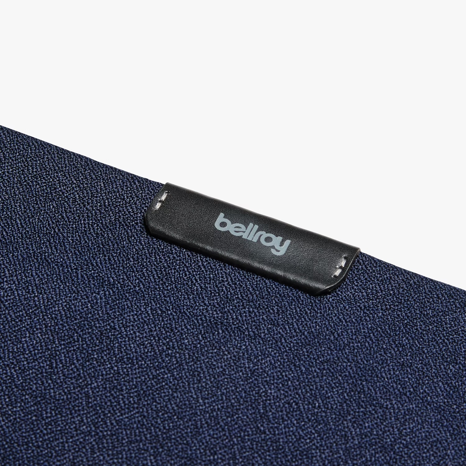 Ciemnoniebieski materiał tekstylny z czarną skórzaną metką z nazwą marki "bellroy".
