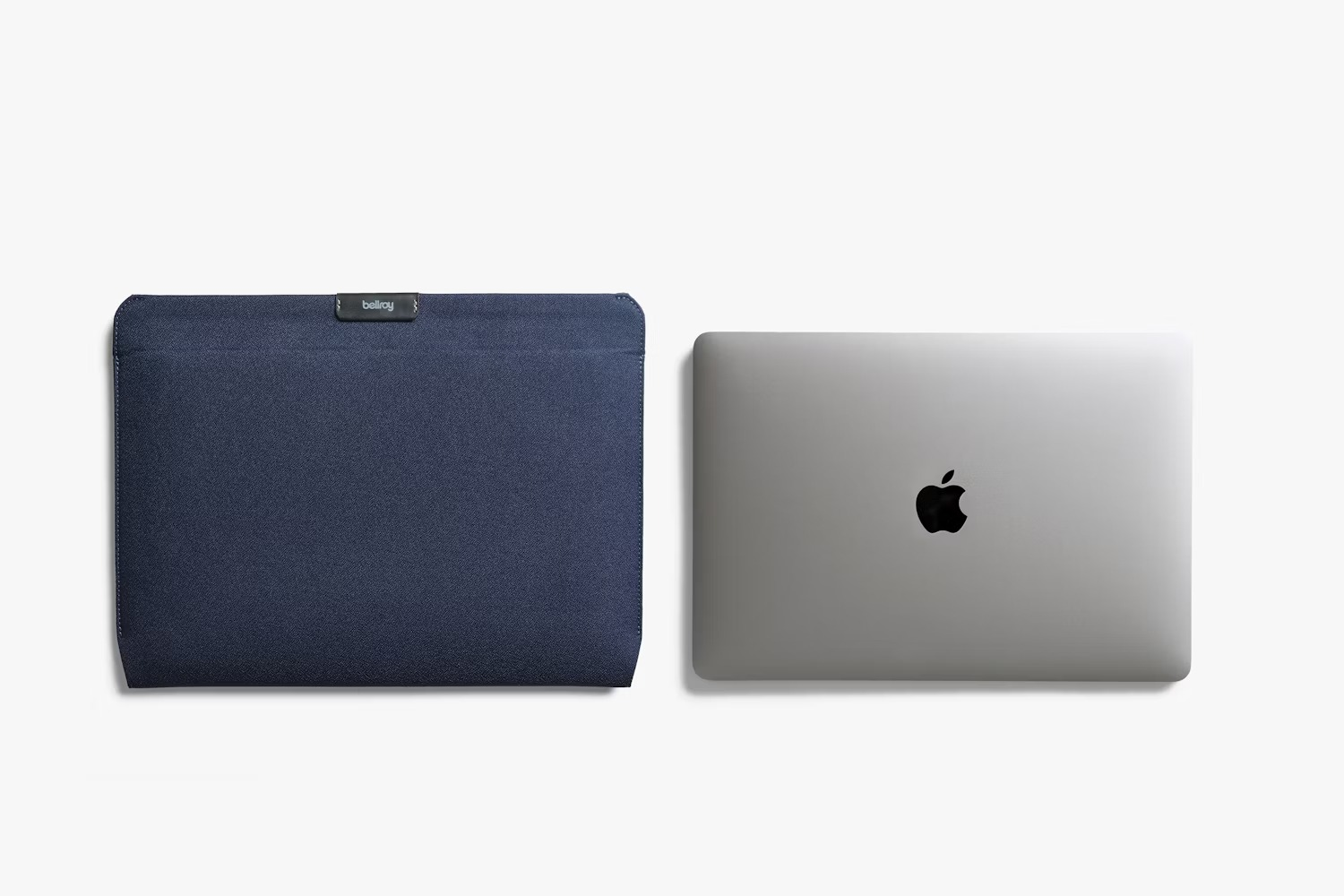 Niebieskie materiałowe etui na laptopa z logo Bellroy obok zamkniętego srebrnego MacBooka.