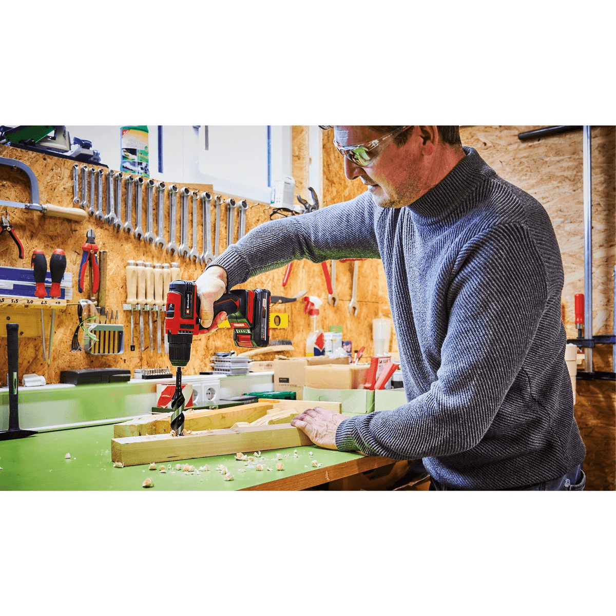Un homme portant des lunettes de protection utilise une perceuse sans fil rouge sur un bloc de bois.