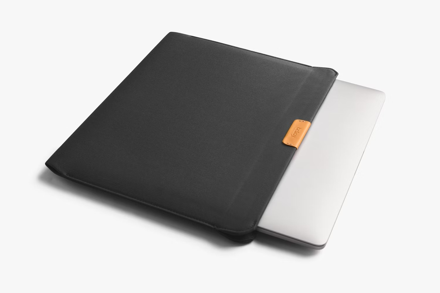Srebrny laptop częściowo w ciemnym etui ochronnym z małą brązową wstawką na białym tle.