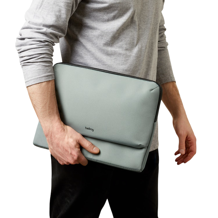 Osoba w szarej koszuli z długim rękawem trzyma szare etui na laptopa Bellroy pod pachą.